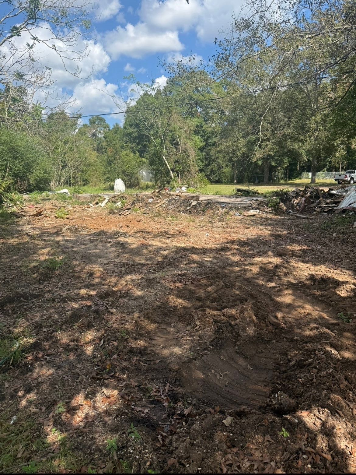 Cleared dirt lot with scattered trees and a partly cloudy sky in the background