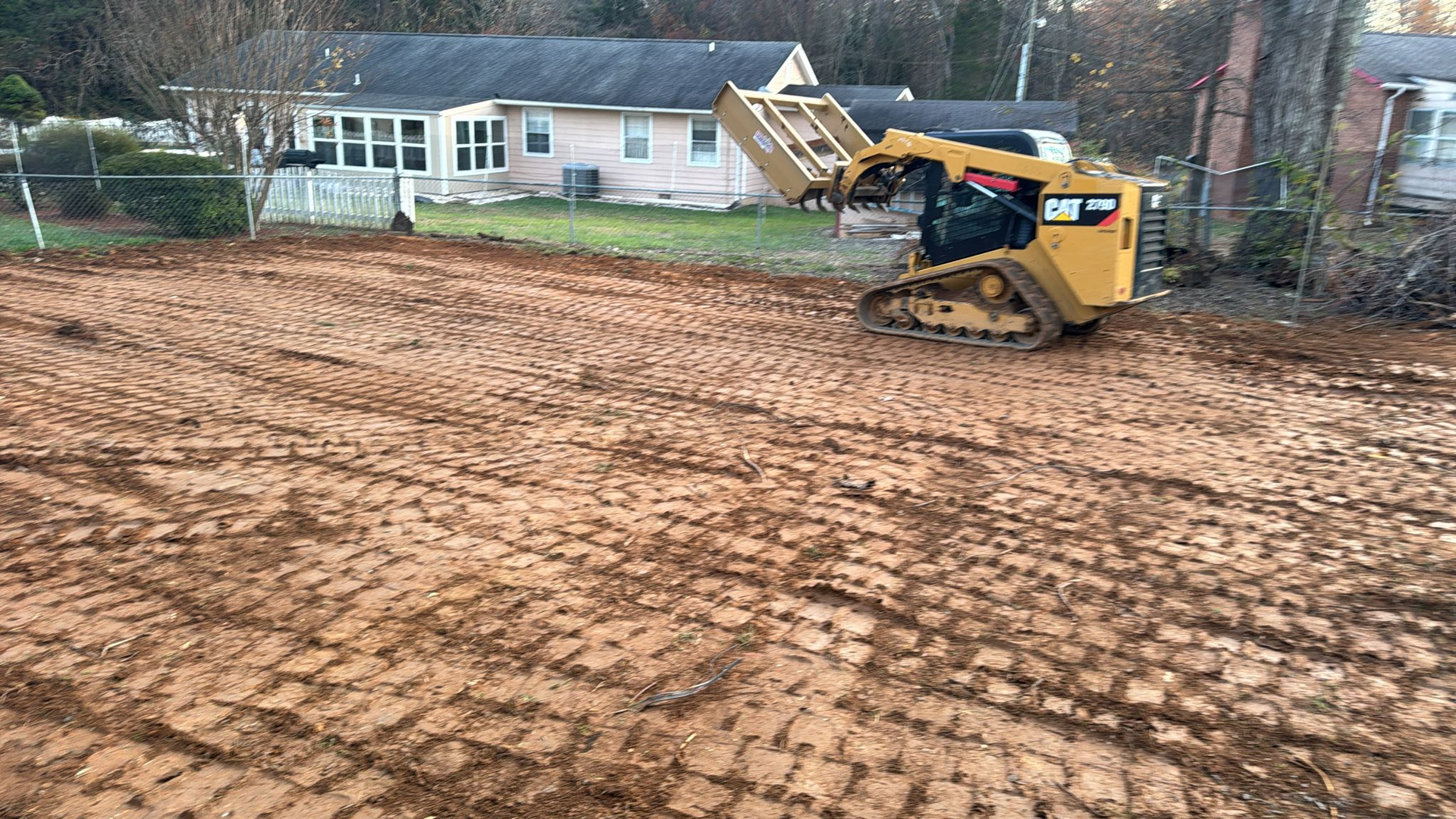 A bulldozer is moving dirt in a muddy field in front of a house.