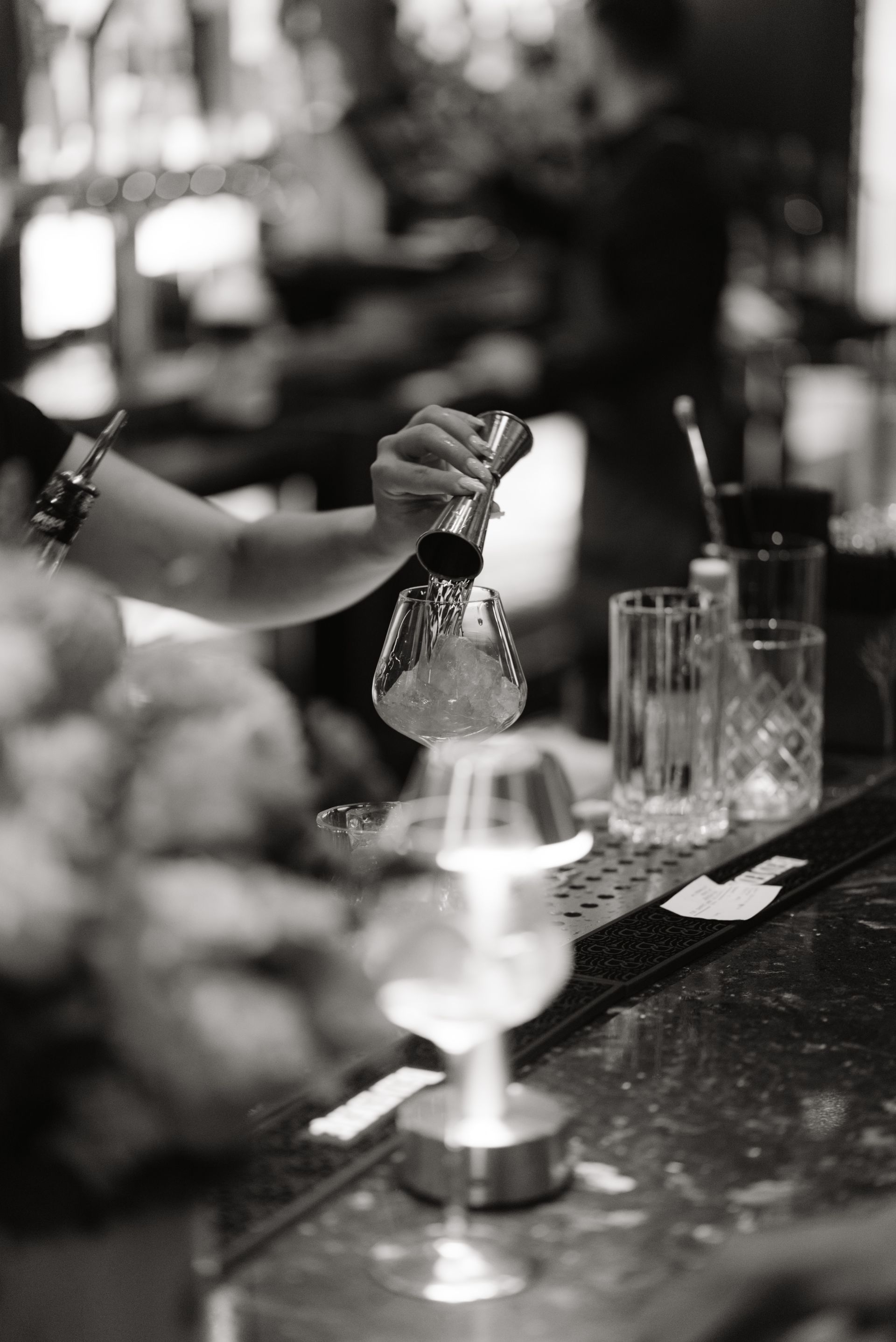 A black and white photo of a bartender pouring a drink into a glass.