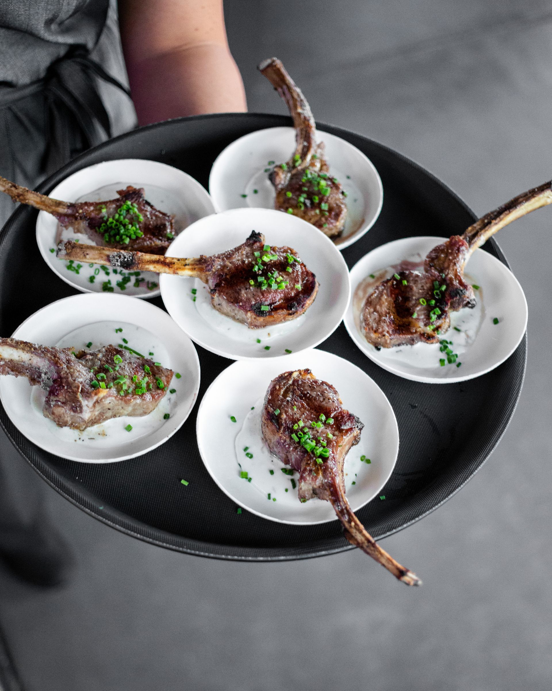 A person is holding a tray of lamb chops on plates