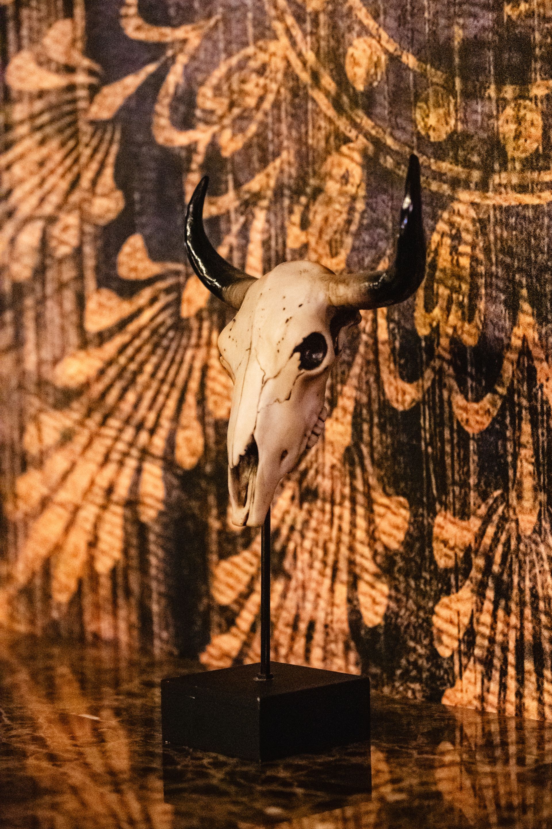 A bull skull on a stand in front of a wall with a pattern.
