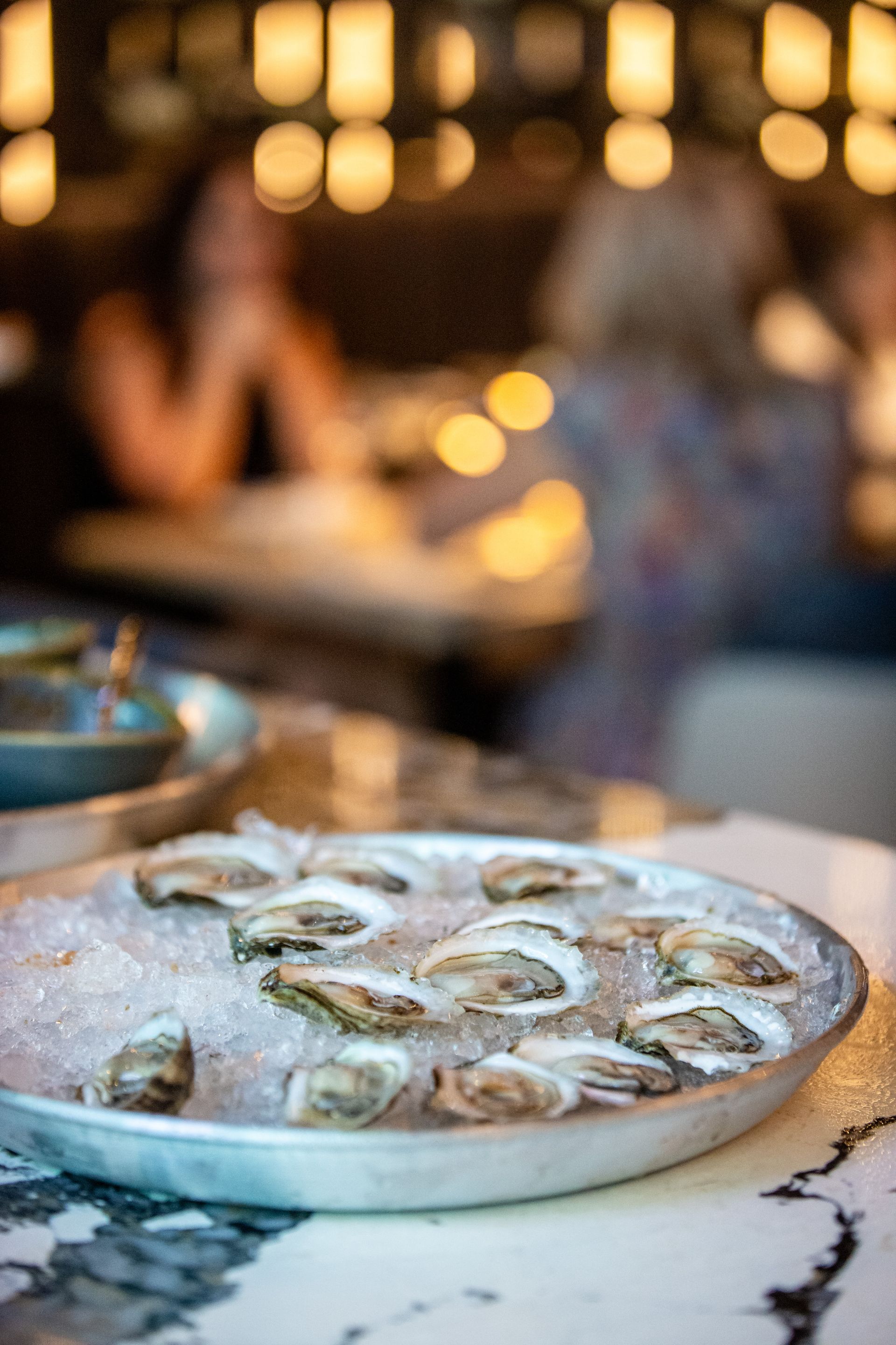 A plate of oysters on ice is on a table in a restaurant.