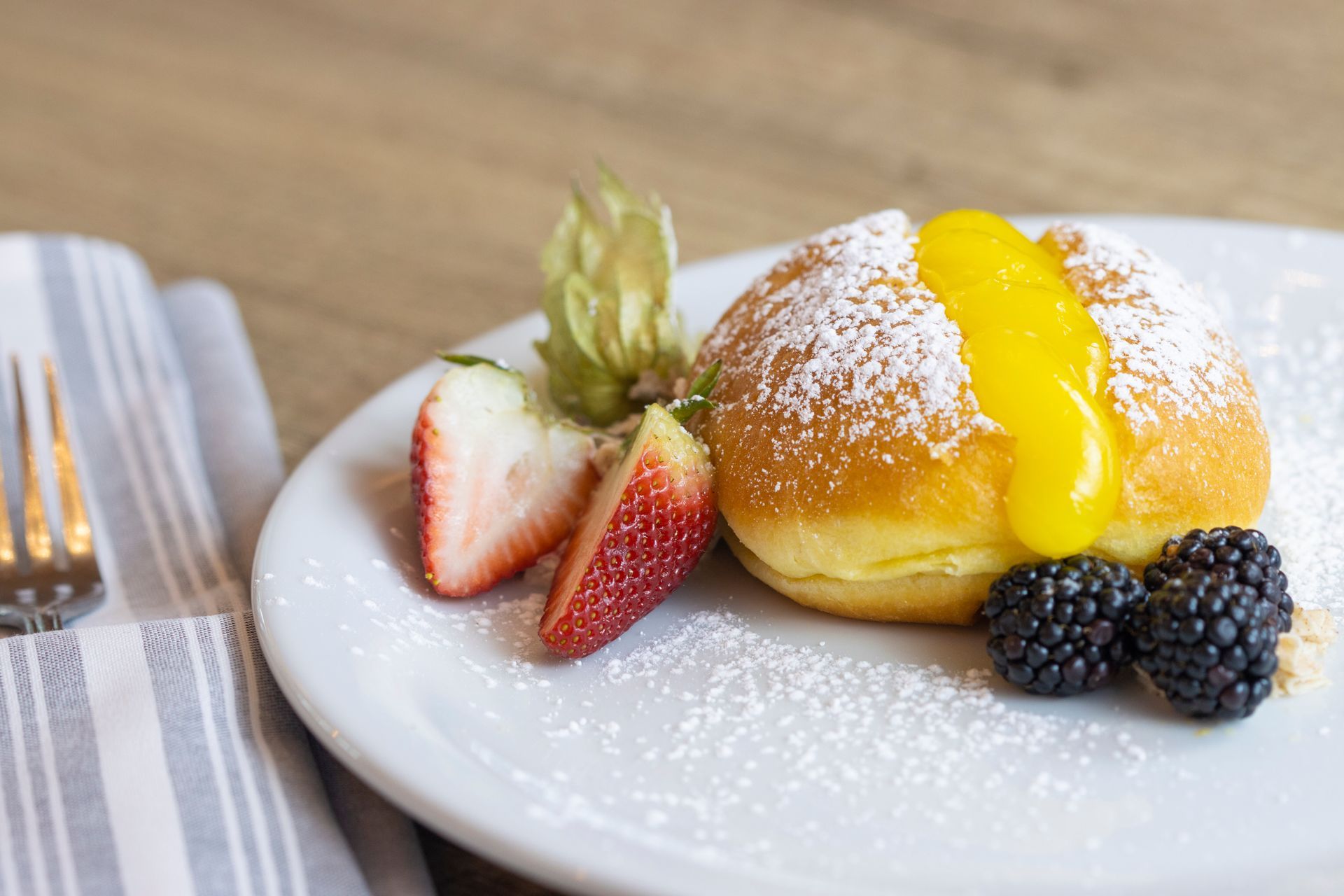 A white plate topped with a donut , berries and powdered sugar.
