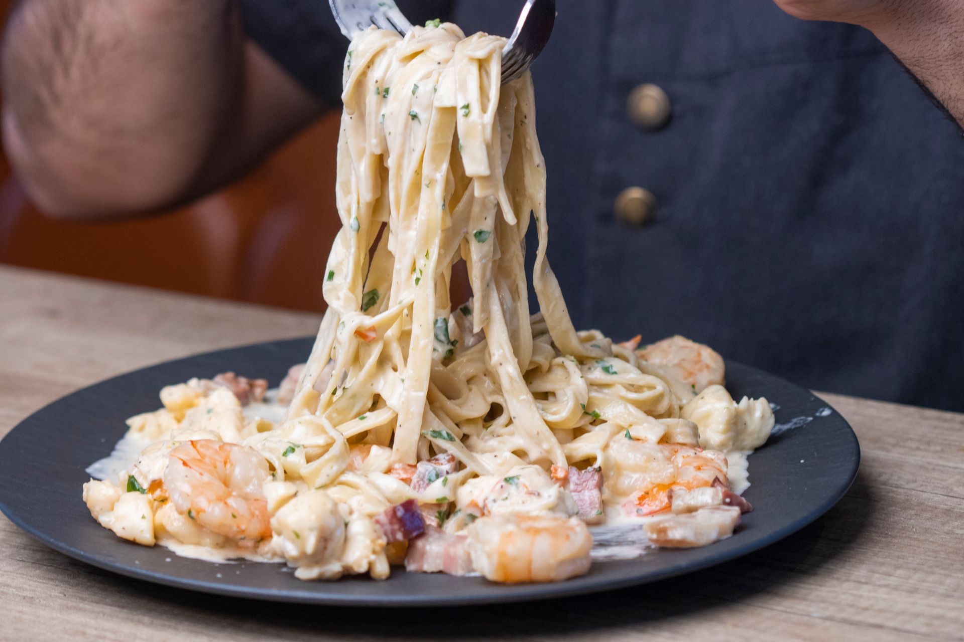 A person is eating pasta with shrimp on a plate with a fork.