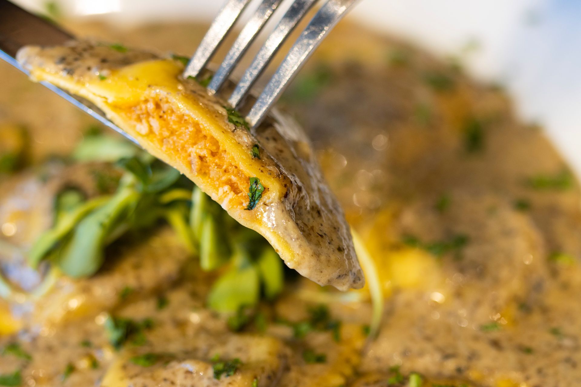 A close up of a fork holding a piece of food over a plate of food.