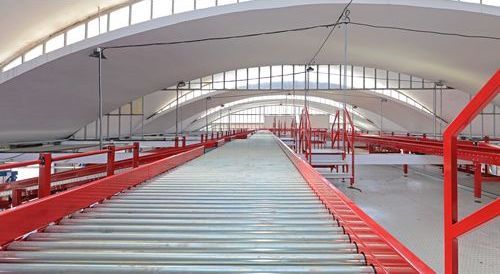 A conveyor belt in a warehouse with a red railing