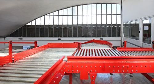 A conveyor belt in a warehouse with a window in the background