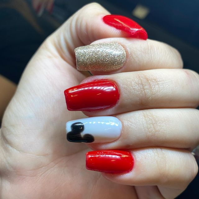 A close up of a woman 's hand with red and gold nails