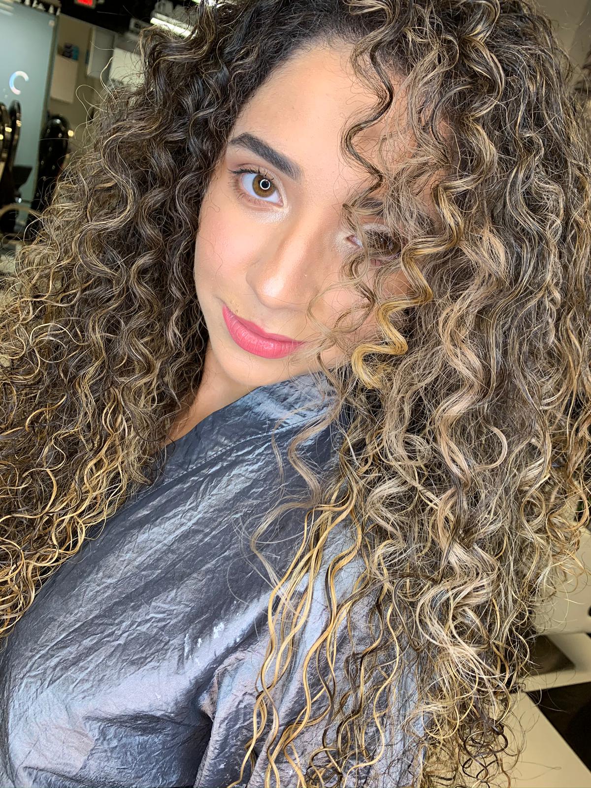 A woman with curly hair is taking a selfie in a salon.