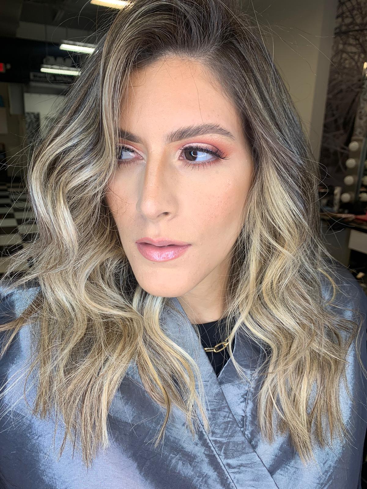 A woman with long blonde hair is wearing a gray jacket and looking at the camera.