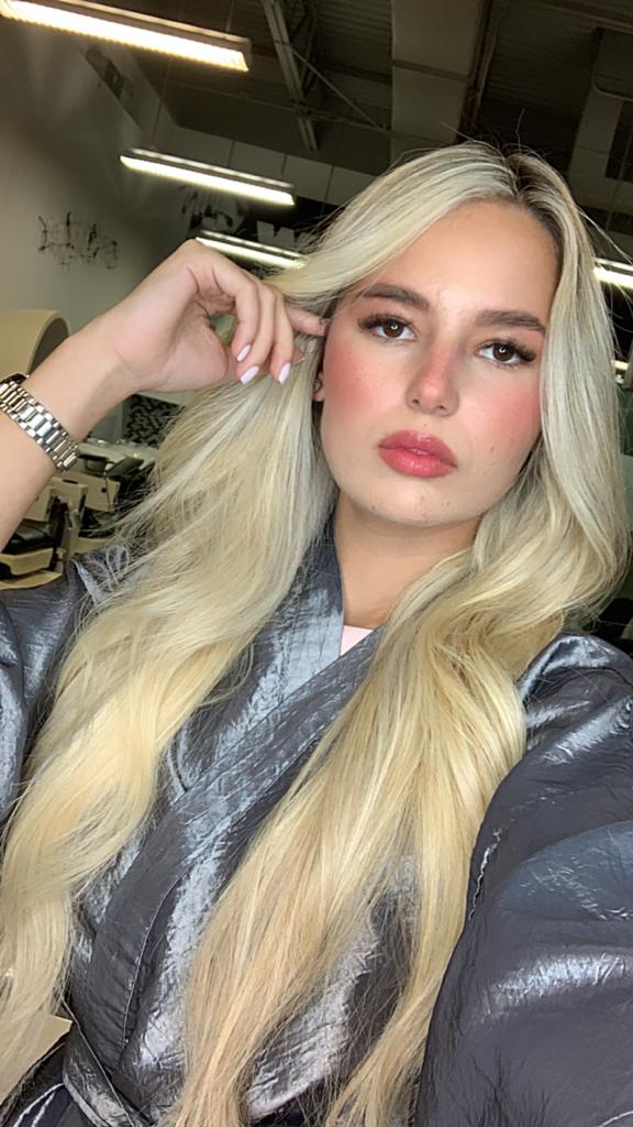 A woman with long blonde hair is taking a selfie in a room.