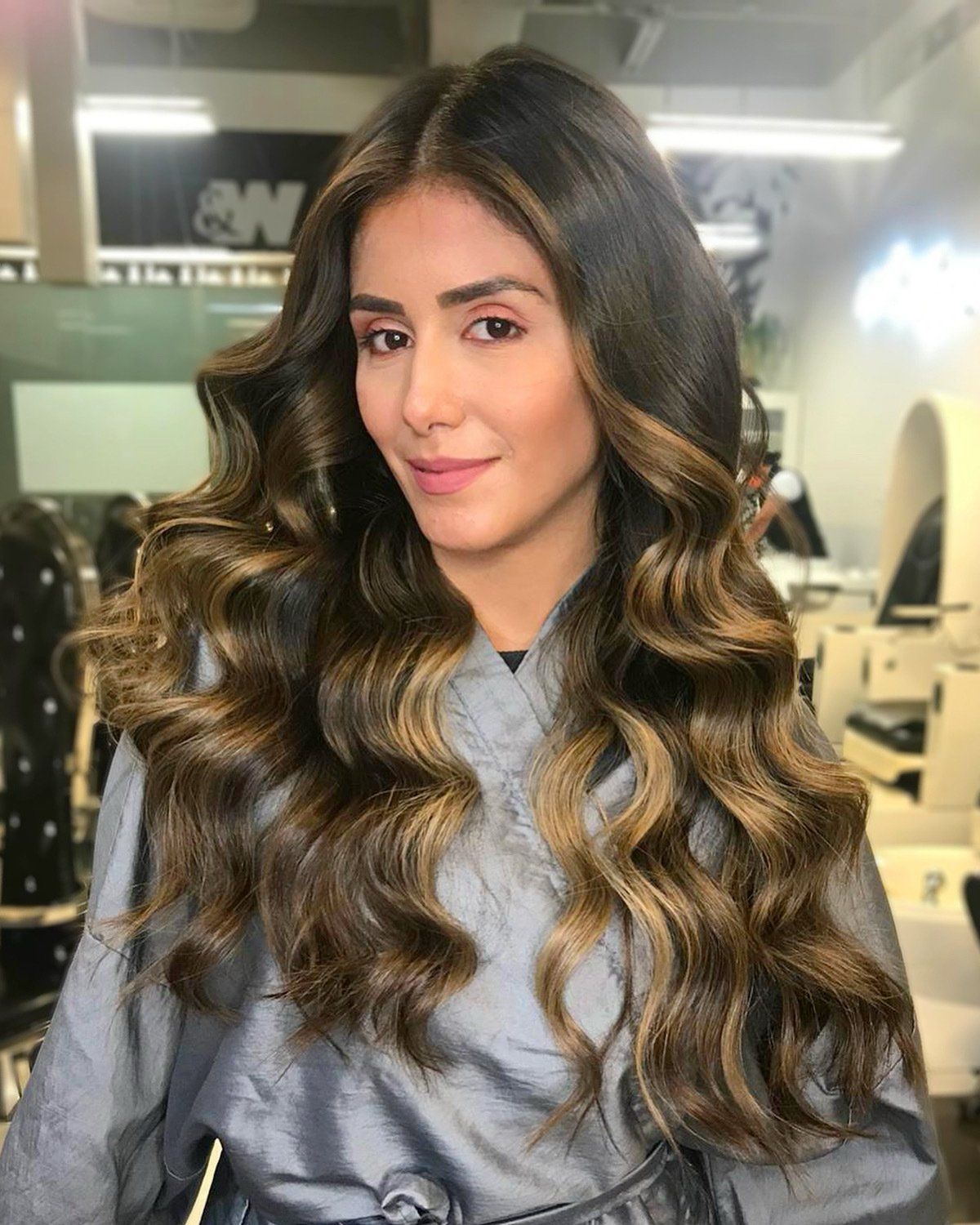 A woman with long wavy hair is standing in a salon.
