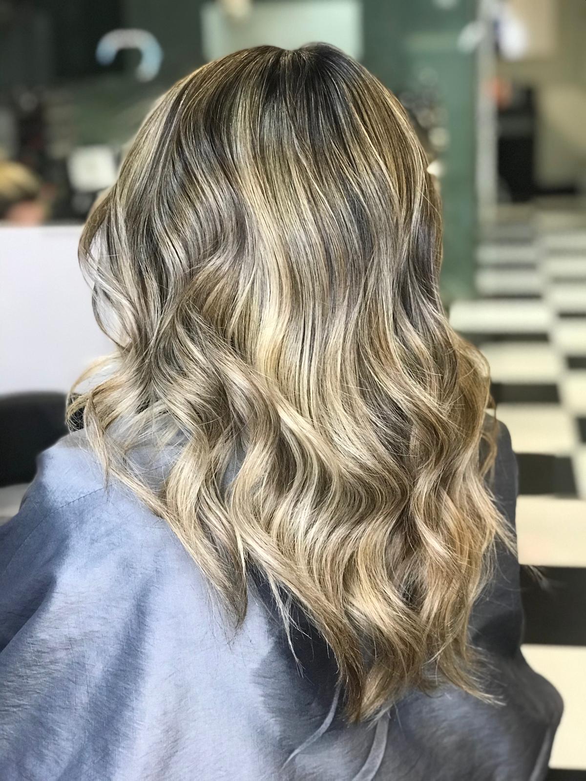A woman with long blonde hair is sitting in a chair in a salon.