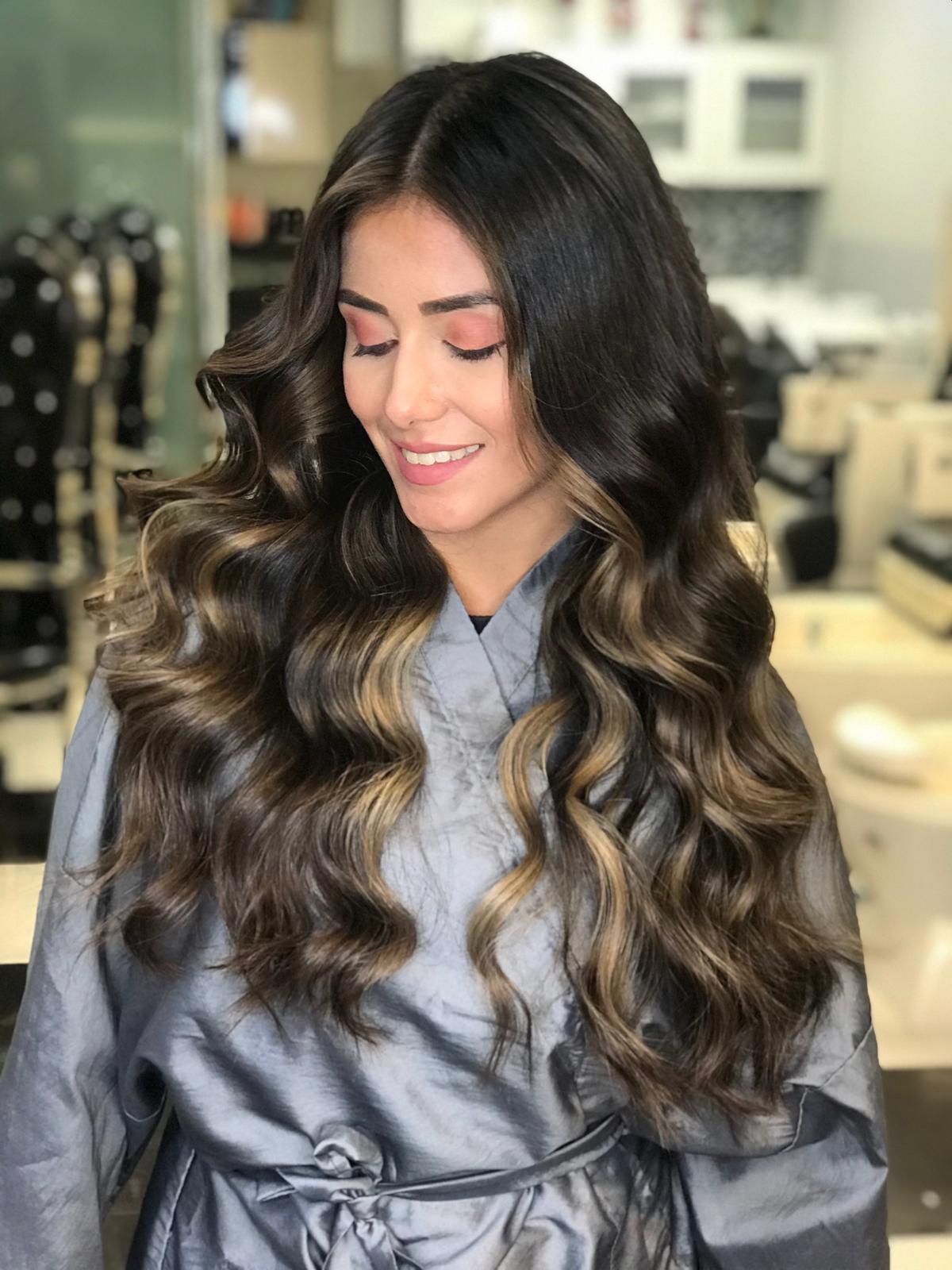 A woman with long wavy hair is smiling in a salon.