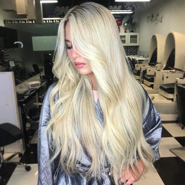 A woman with long blonde hair is standing in a salon
