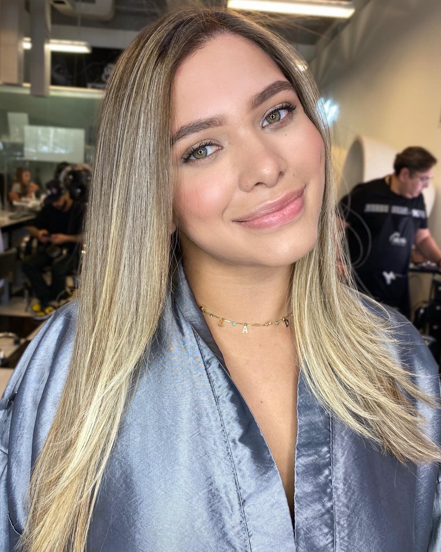 A woman with blonde hair is wearing a grey robe and smiling