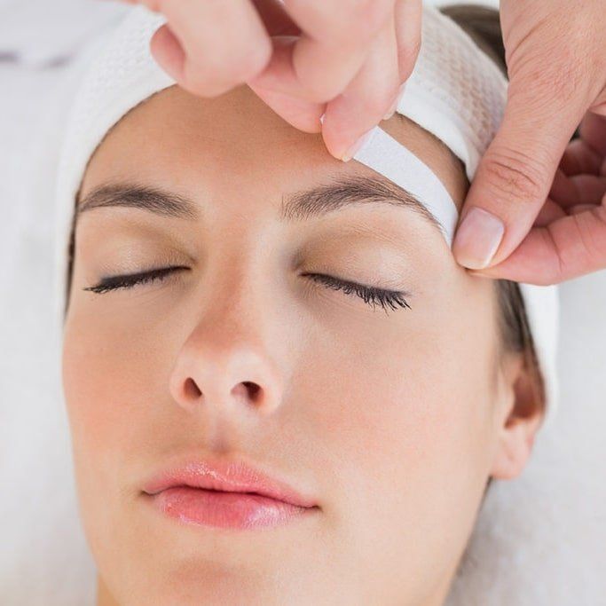 A woman with her eyes closed is getting her eyebrows waxed