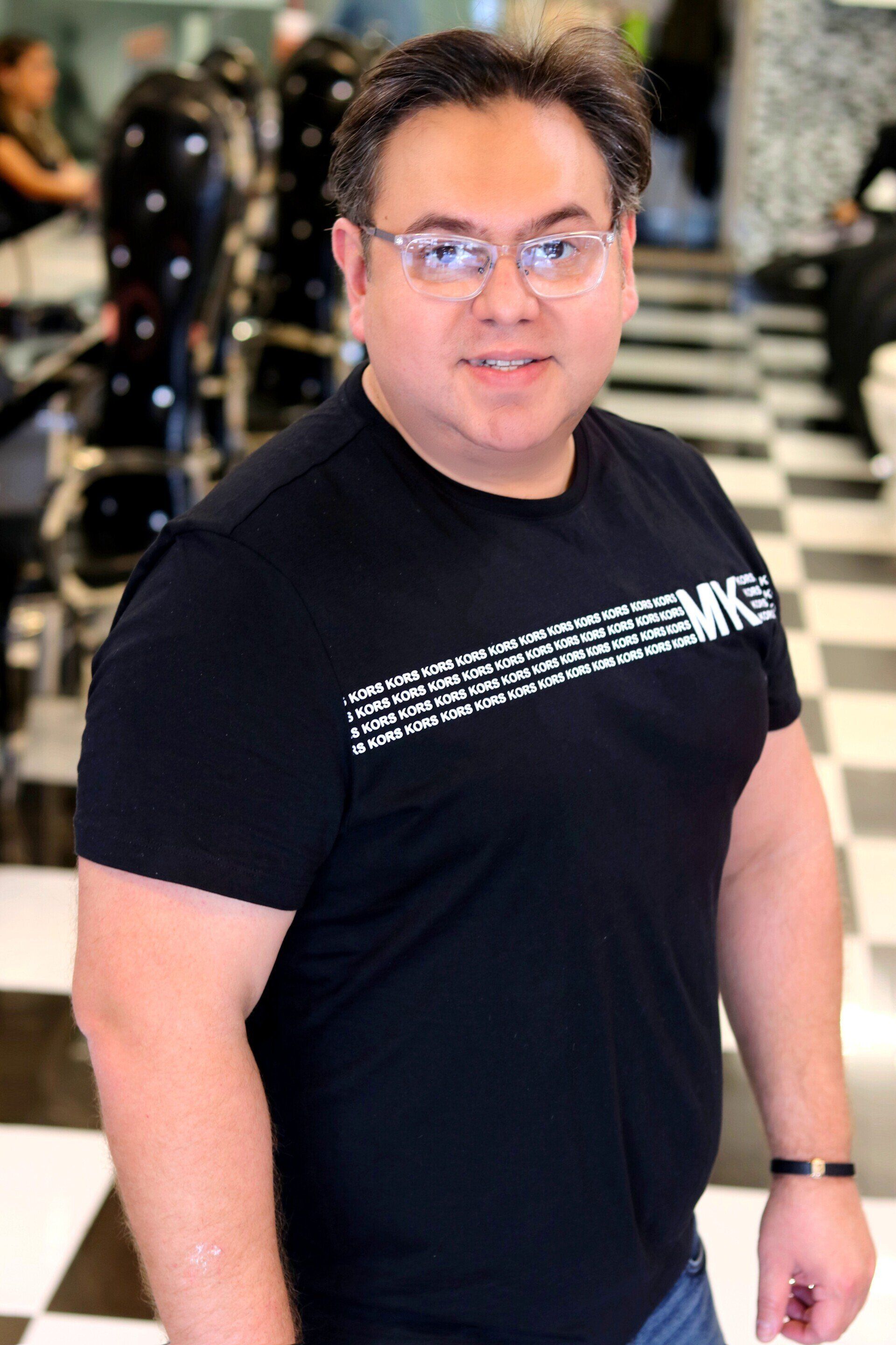 A man wearing glasses and a black shirt is standing in a barber shop.