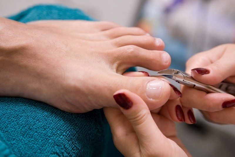 A person is getting their toenails cut with scissors.