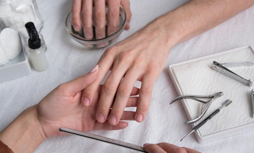 A woman is giving a man a manicure at a nail salon.