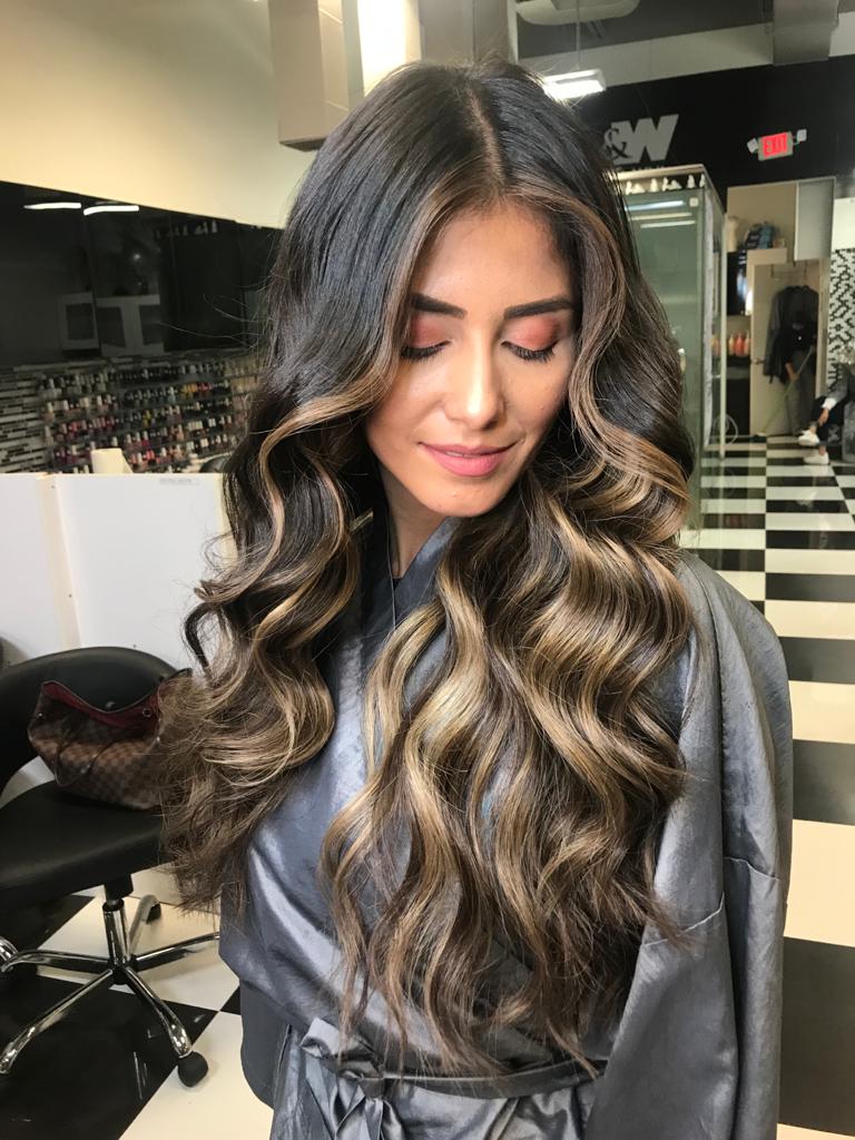 A woman with long hair is standing in a salon with her eyes closed.