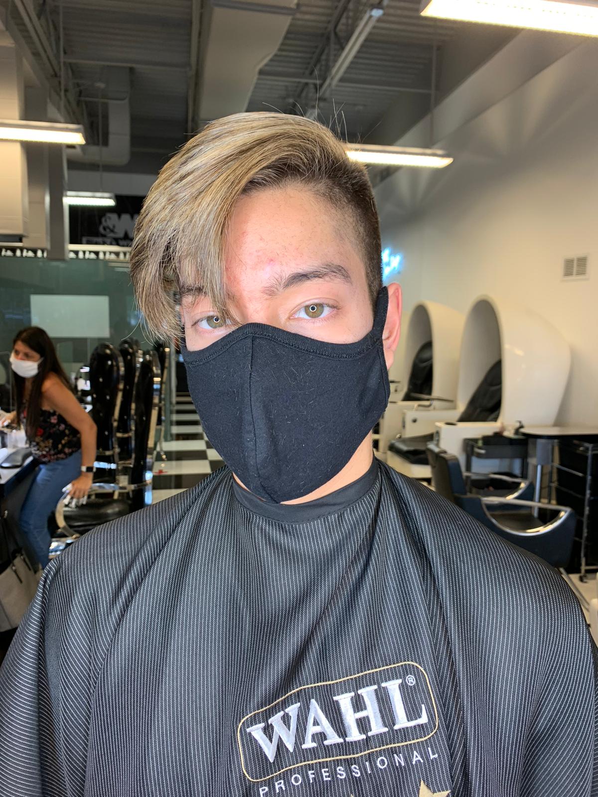 A man wearing a black wahl apron is getting his hair cut