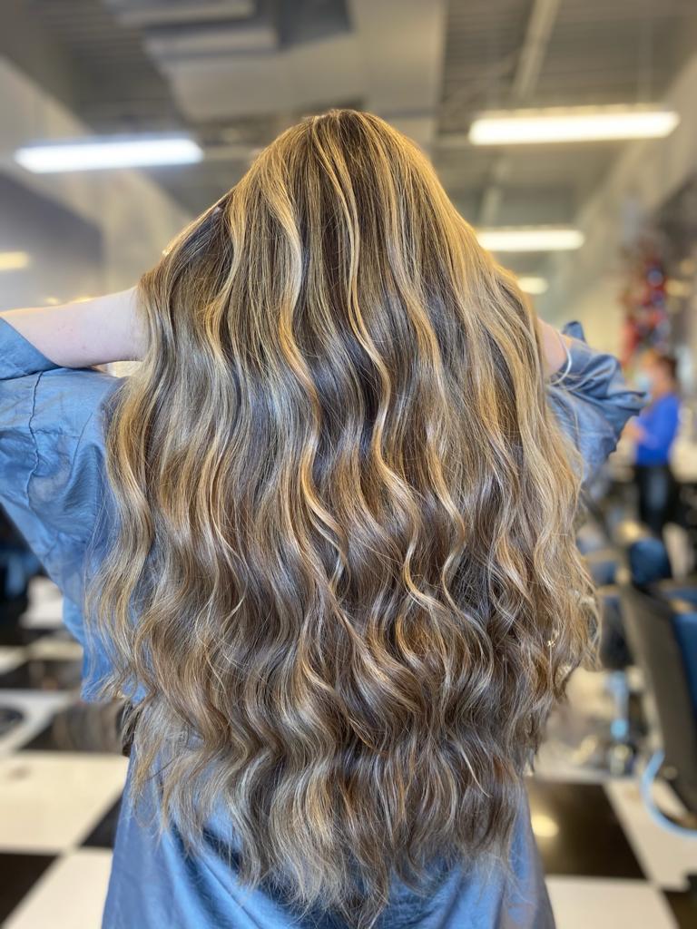 A woman with long blonde hair is standing in a salon with her hands behind her head.