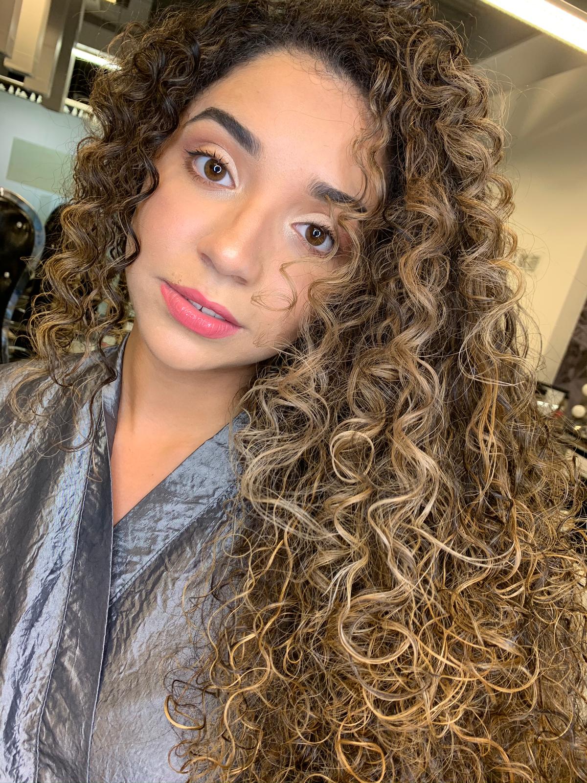 A woman with curly hair is taking a selfie in a salon.