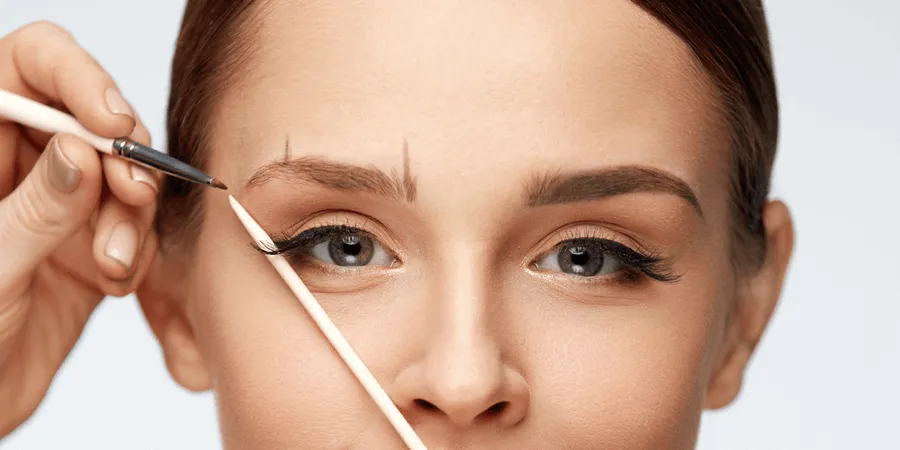 A woman is measuring her eyebrows with a pencil.