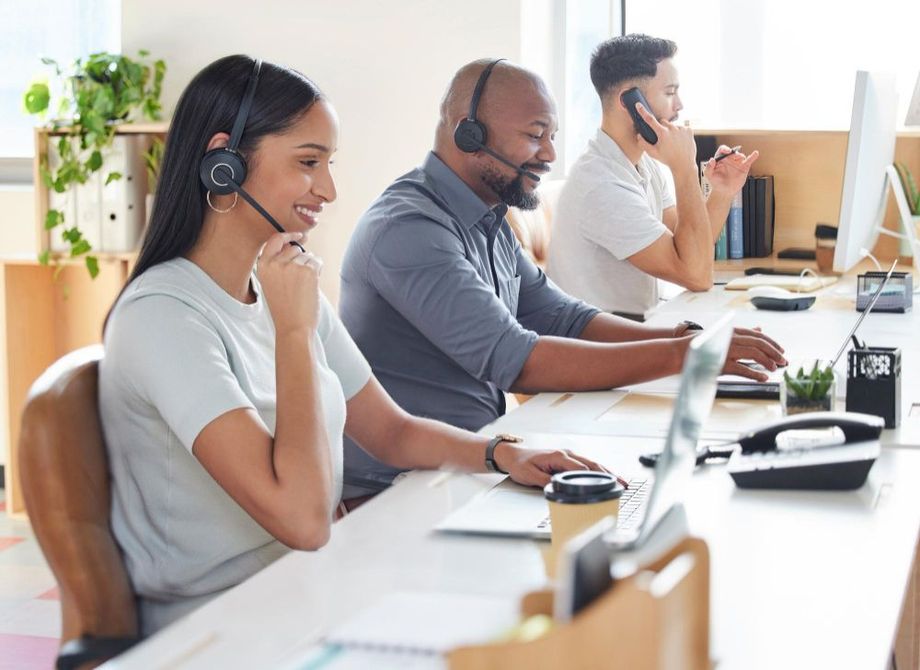 A group of people are sitting at desks in a call center wearing headsets.