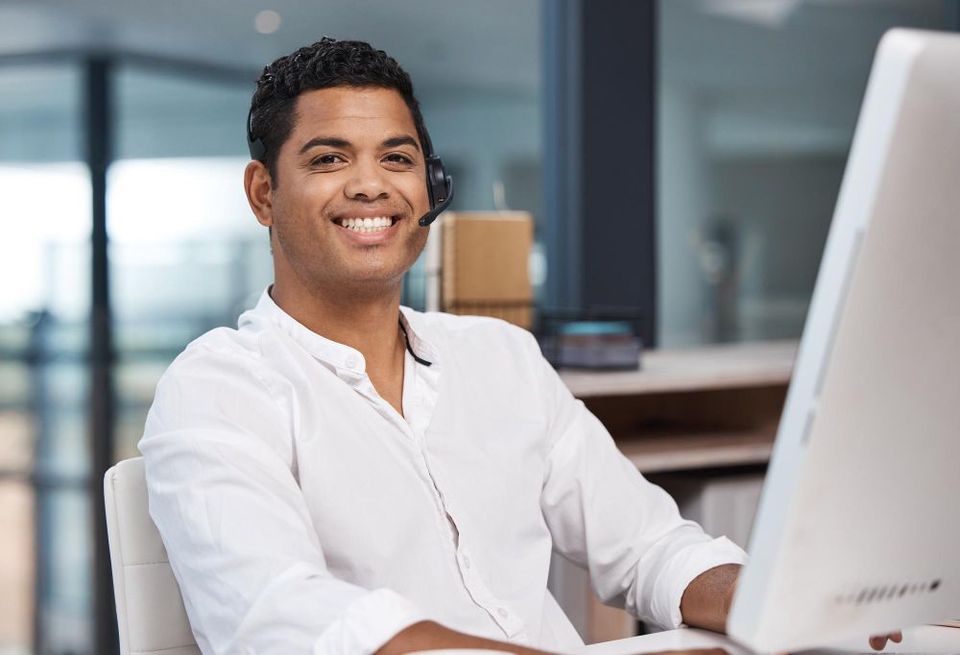 A man wearing a headset is smiling while sitting in front of a computer.