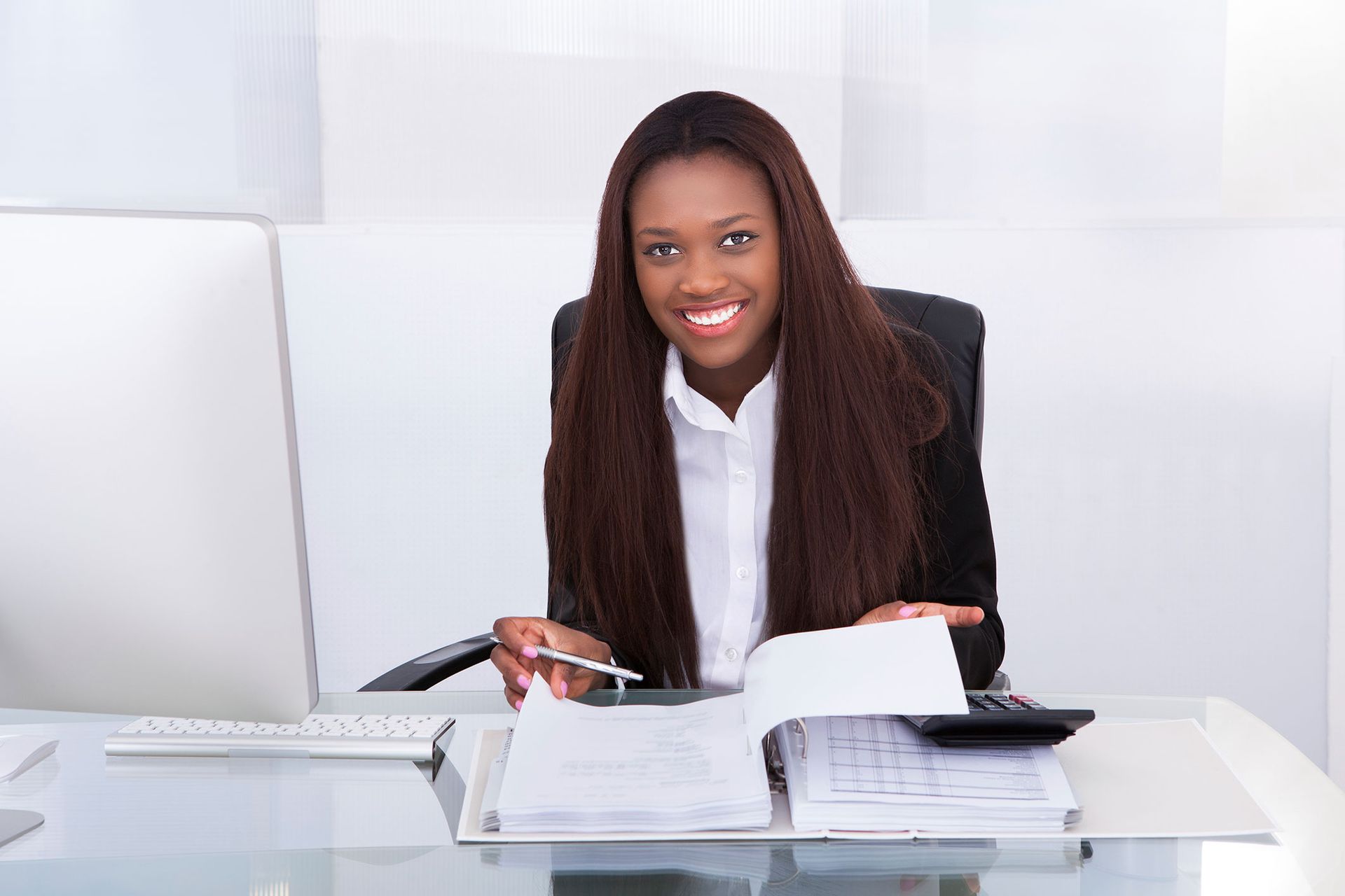 A woman is sitting at a desk with a calculator and a pen.