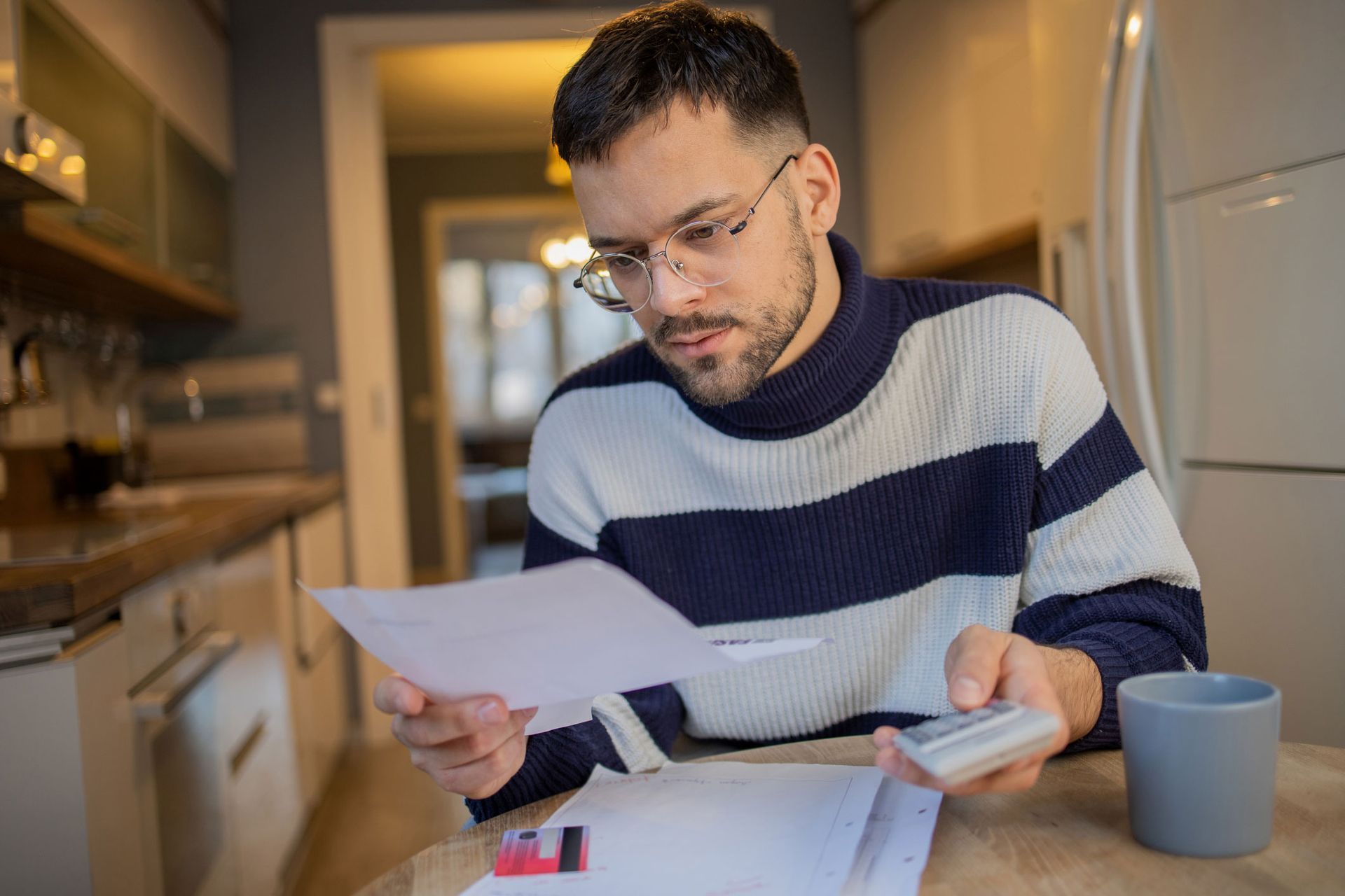 A man is sitting at a table holding a piece of paper and a calculator.