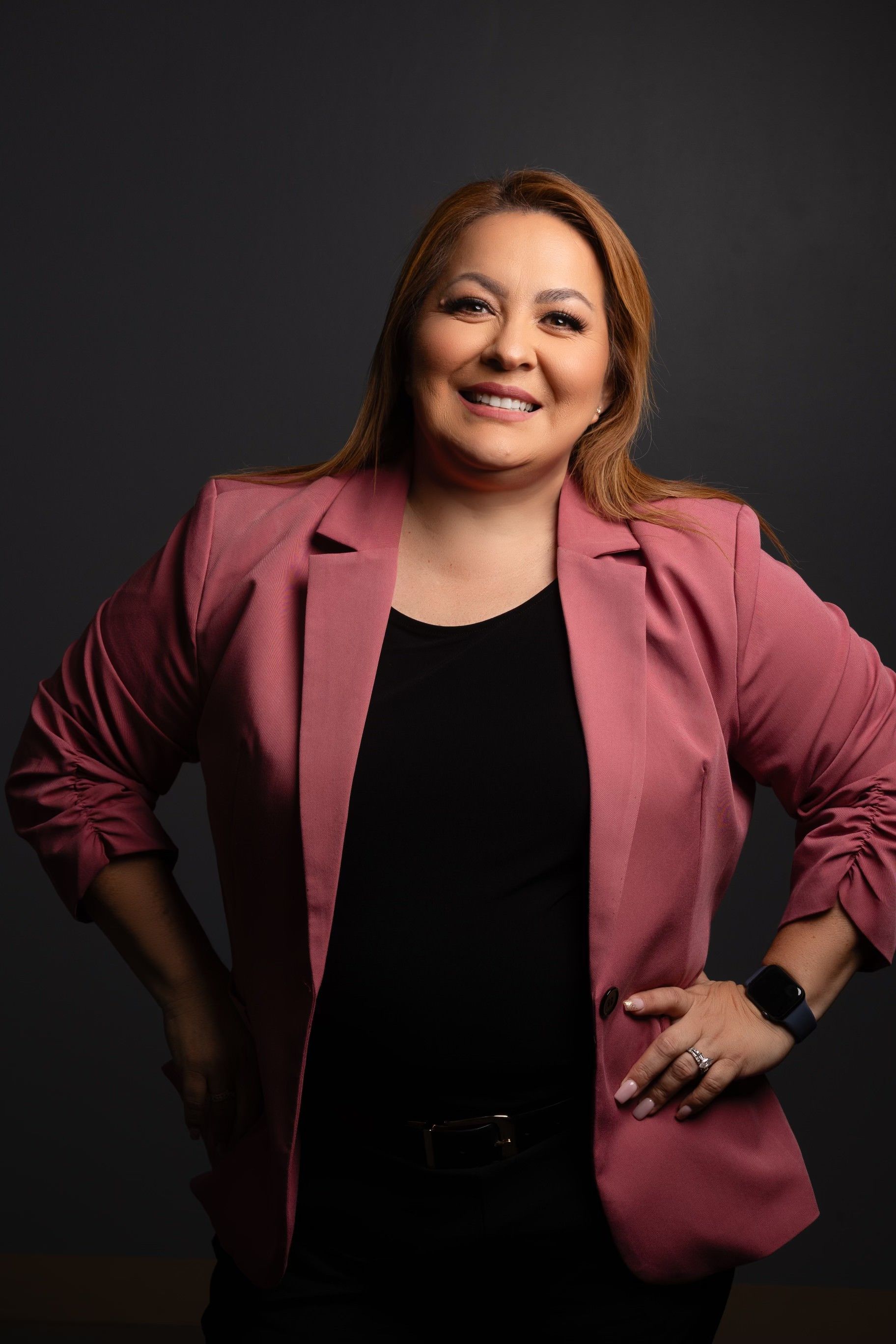 A woman wearing a pink jacket and a black shirt is standing with her hands on her hips.