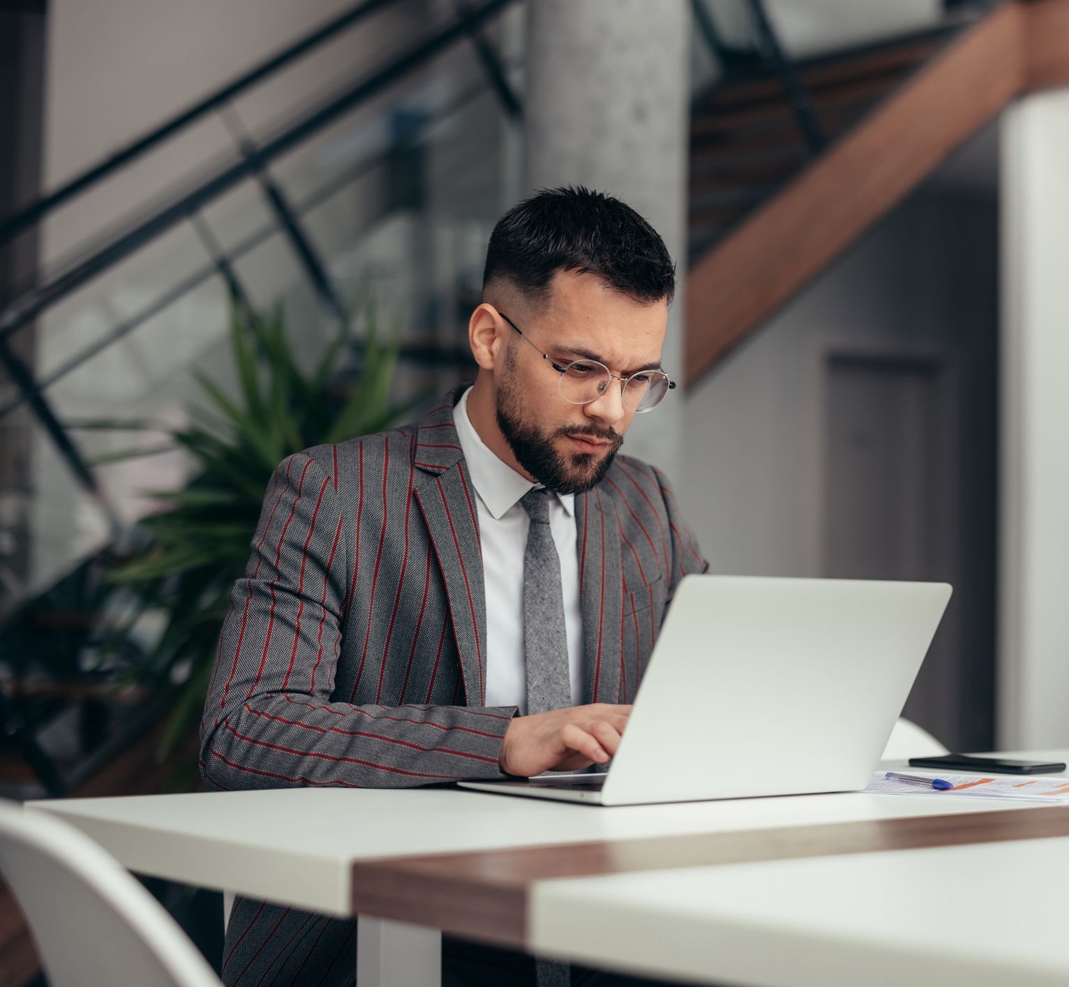 A man in a suit and tie is sitting at a table using a laptop computer.