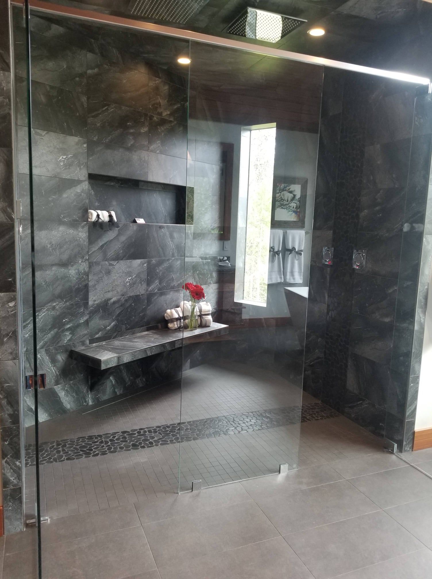 Modern bathroom with dark gray stone walls, glass shower door, and built-in bench.