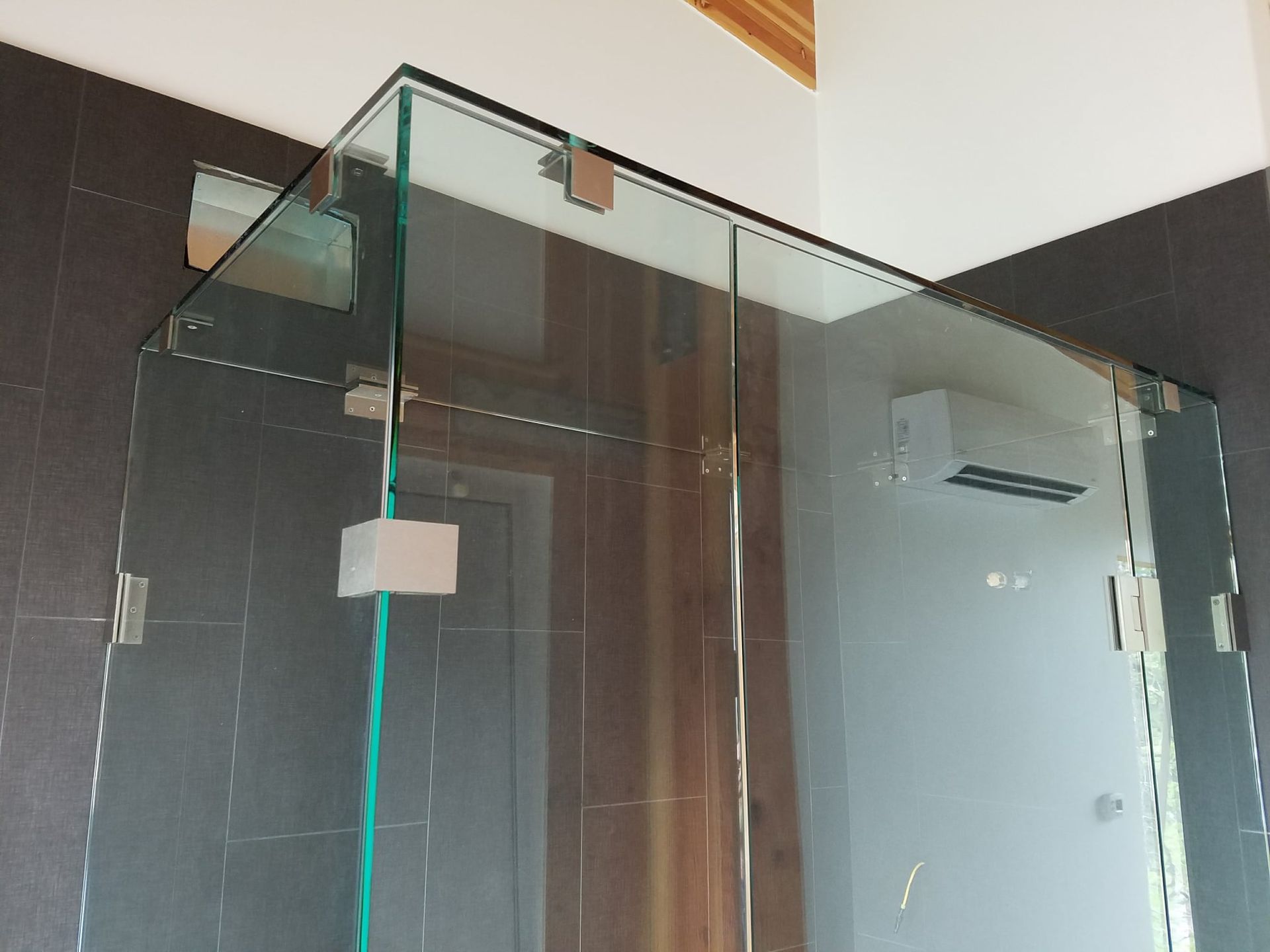 Glass shower enclosure with wall-mounted brackets; gray and wooden walls visible.