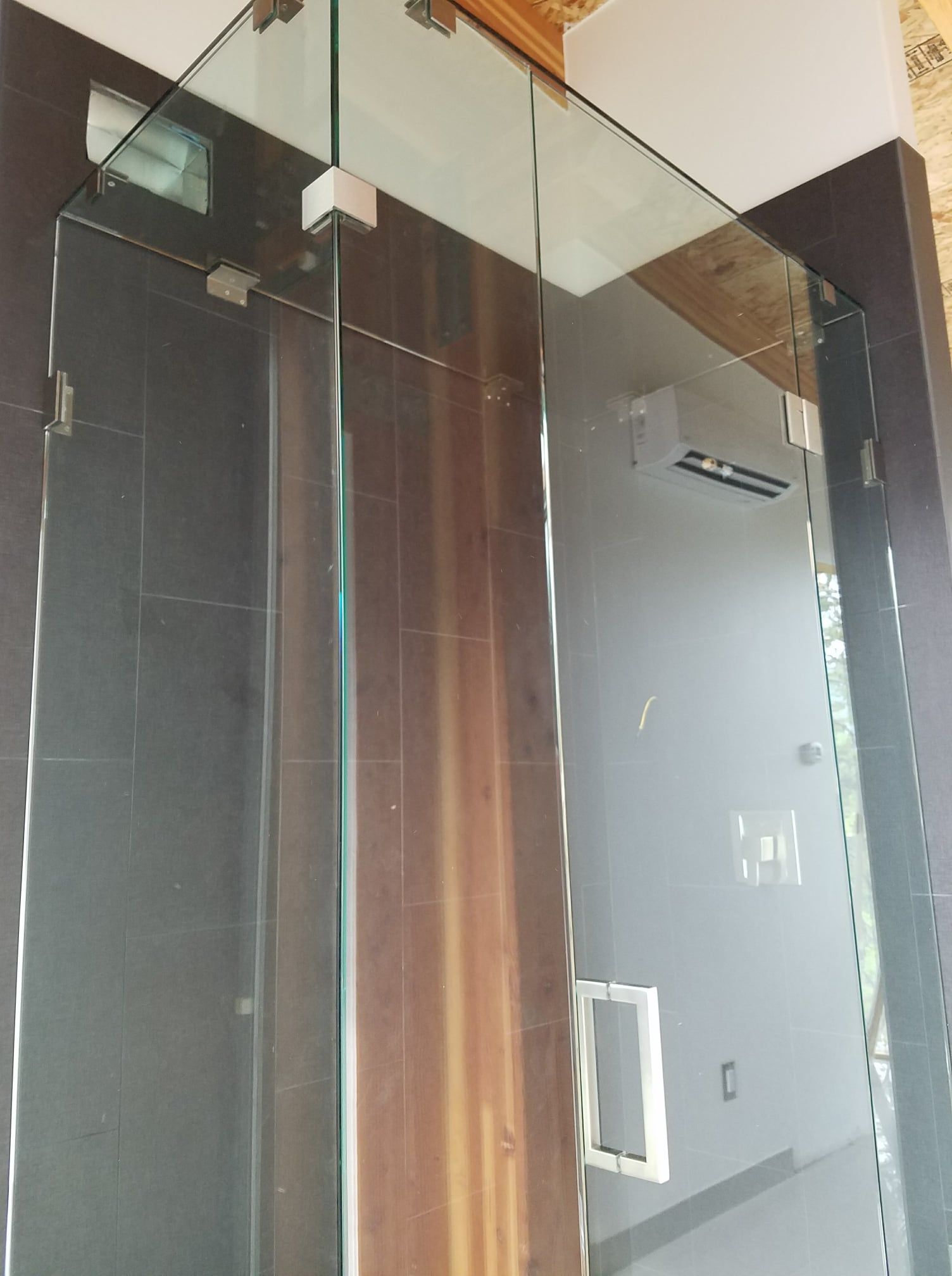 Glass shower enclosure with chrome hardware, on dark tile walls, and wood accent.