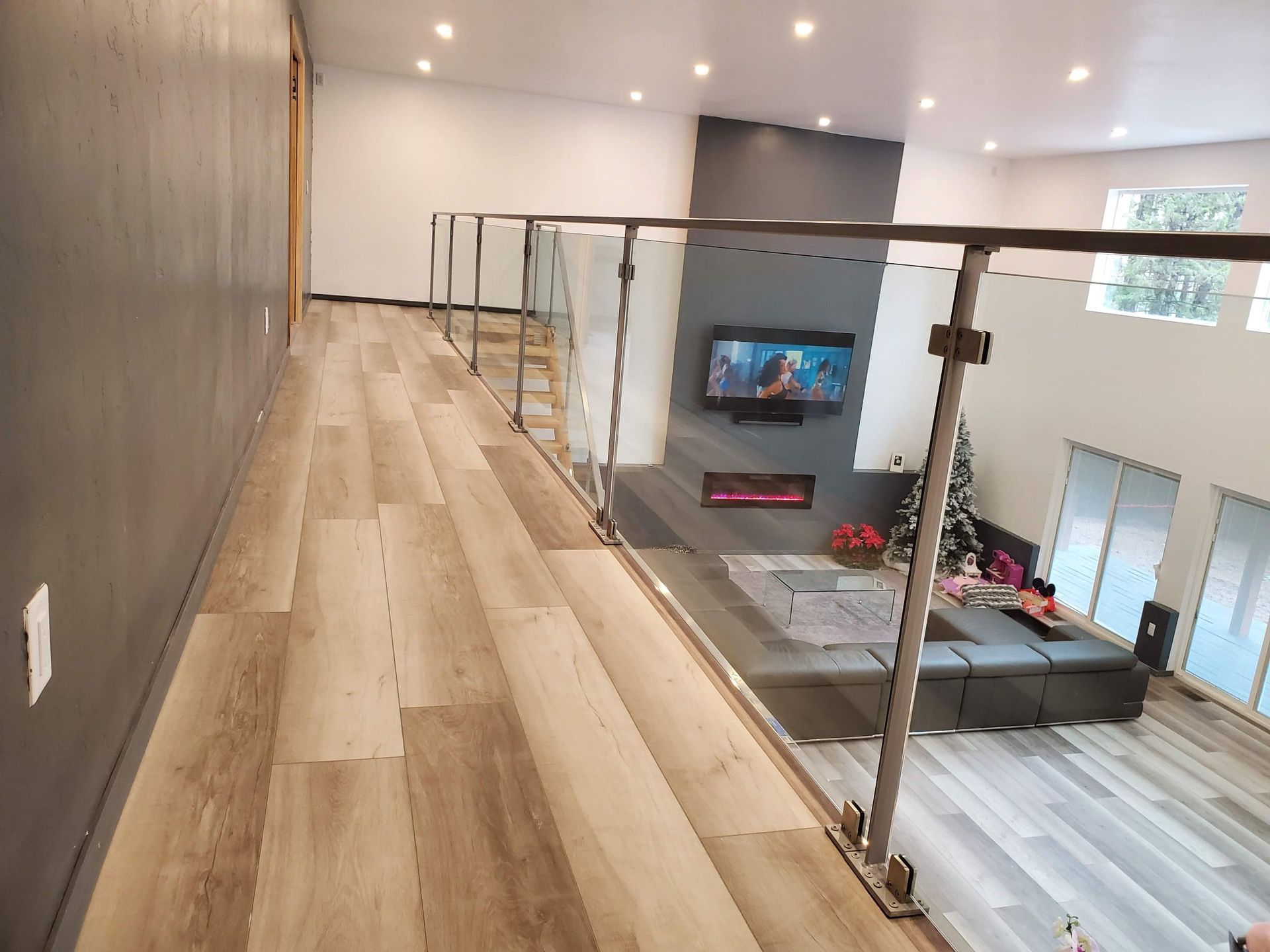 A modern loft with glass railings overlooking a living room with a fireplace, TV, and sectional sofa.