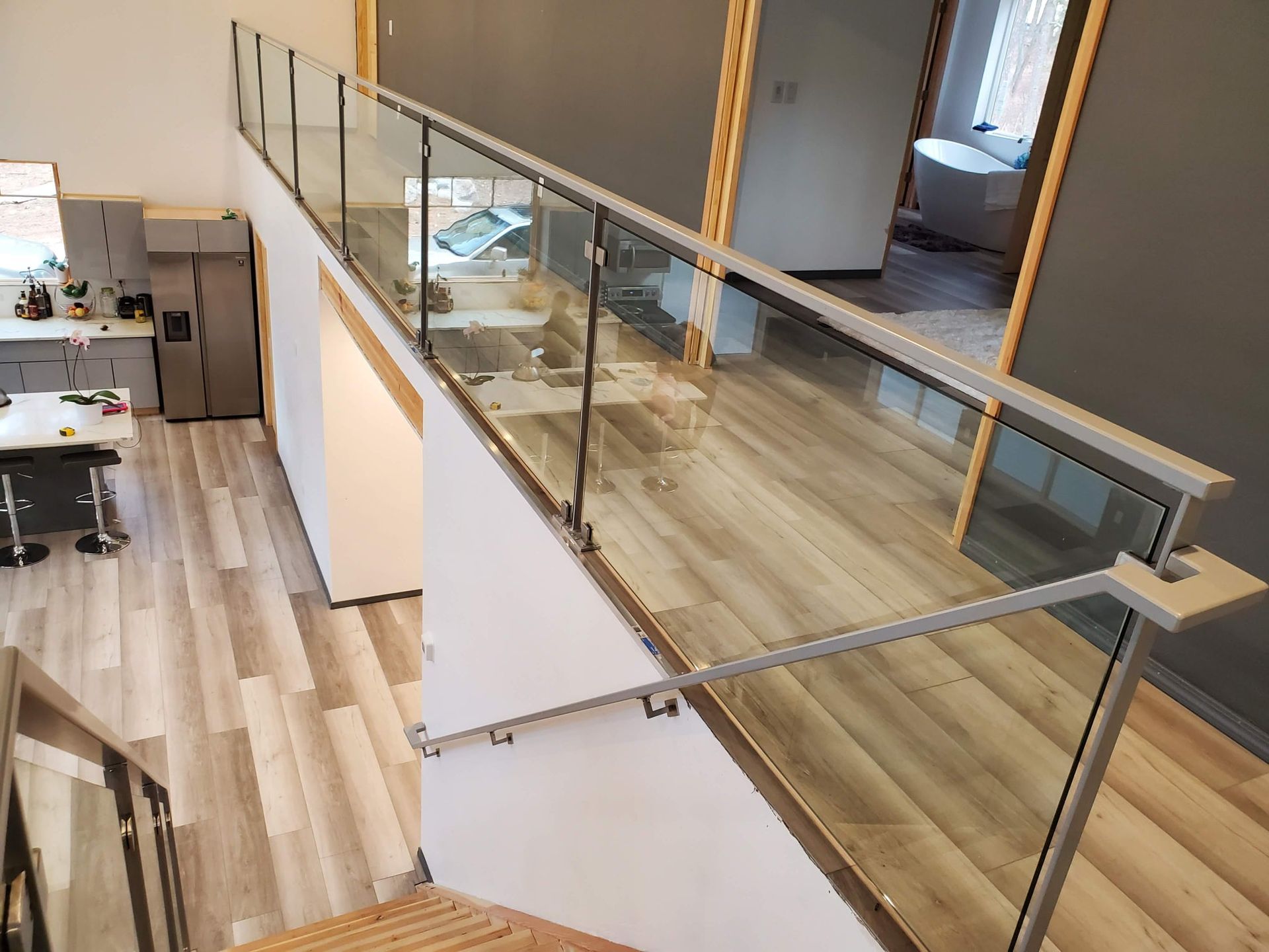 Modern interior with glass railing, light wood floors, and a kitchen area visible.