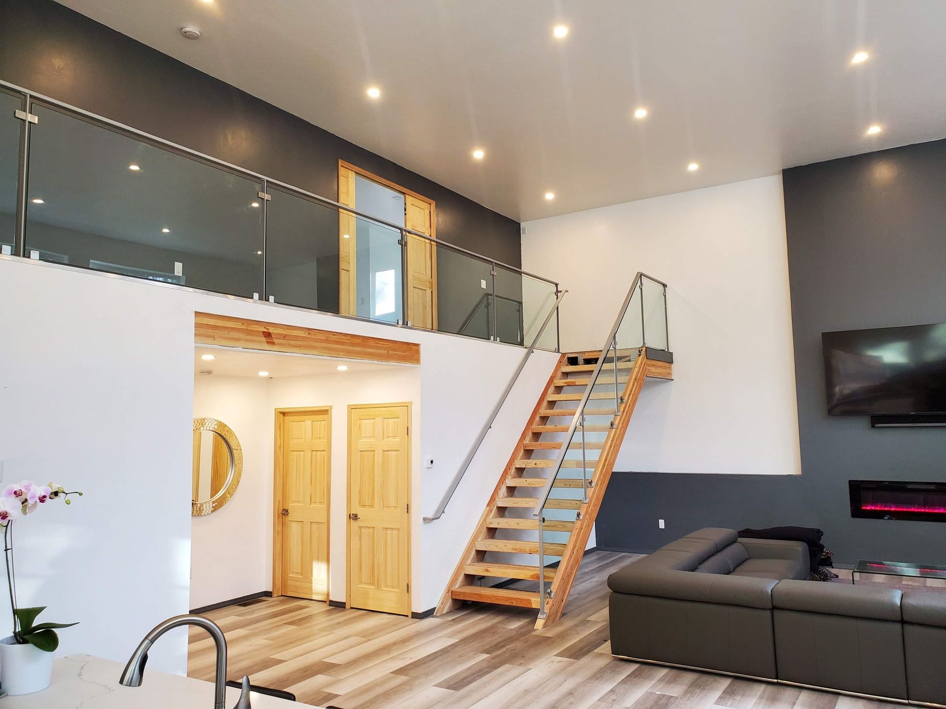 Modern loft interior with a staircase, glass railings, and dark grey accent wall.