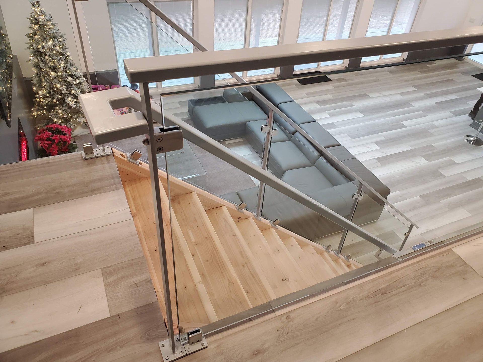 Staircase with wooden steps, glass panels, and metal railings. A grey sectional sofa sits nearby.