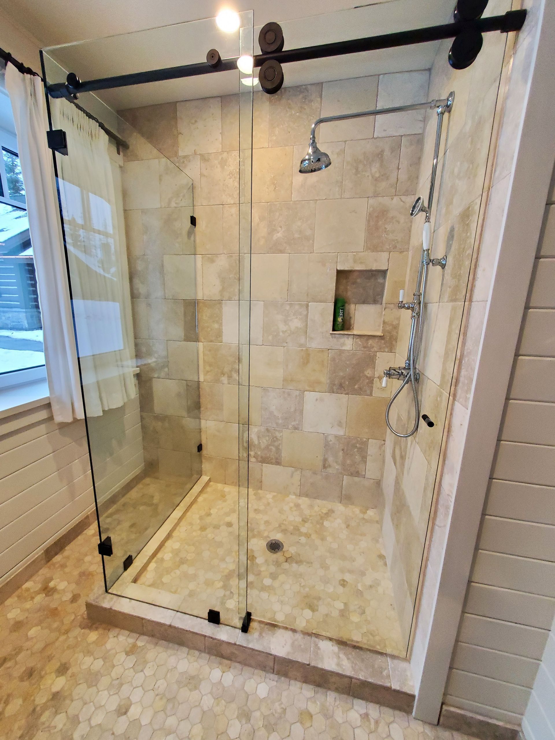 Glass-enclosed shower with beige tile walls, a glass bench, and a silver showerhead.
