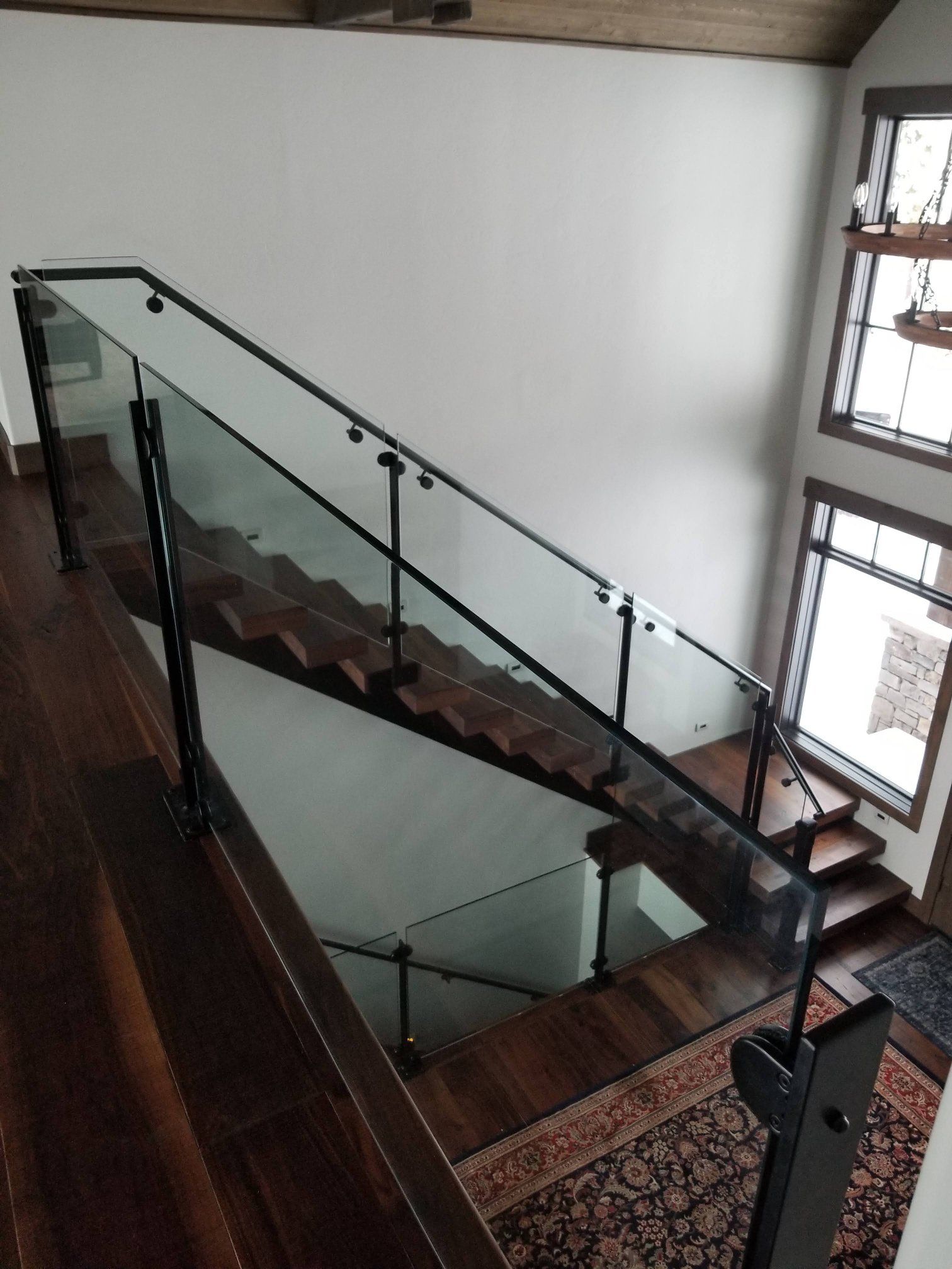 Staircase with dark wood steps and glass railing with black metal supports.