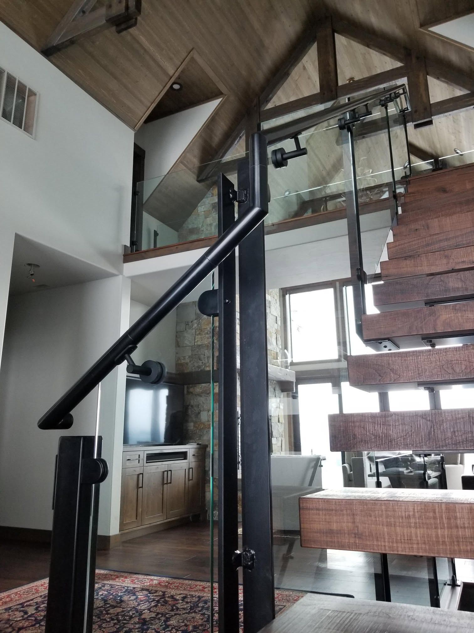 Interior view of a staircase with wood and metal features, a black handrail, and a view to a second floor.