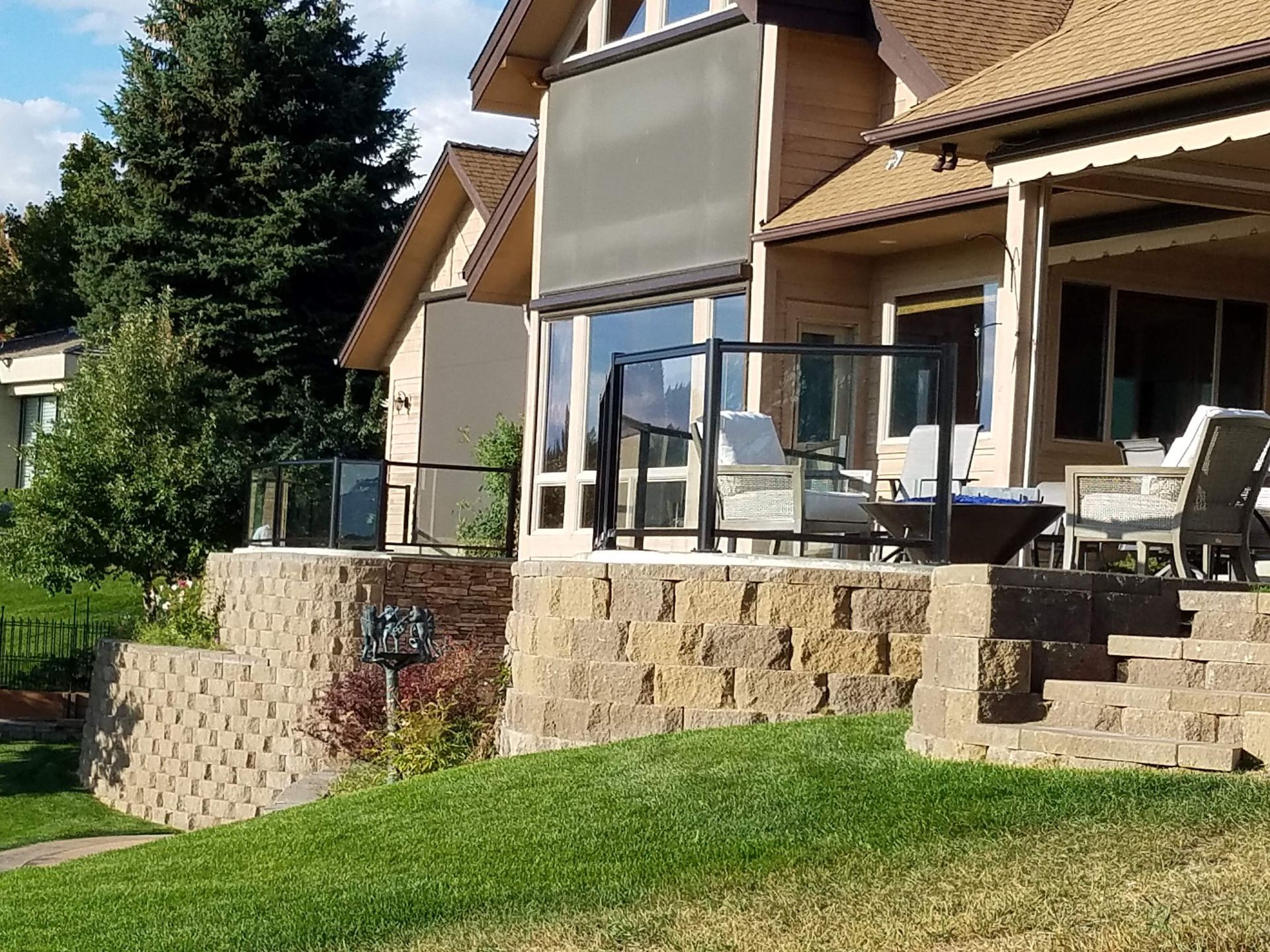 House exterior with a tiered brick retaining wall, glass railing, and green grass.