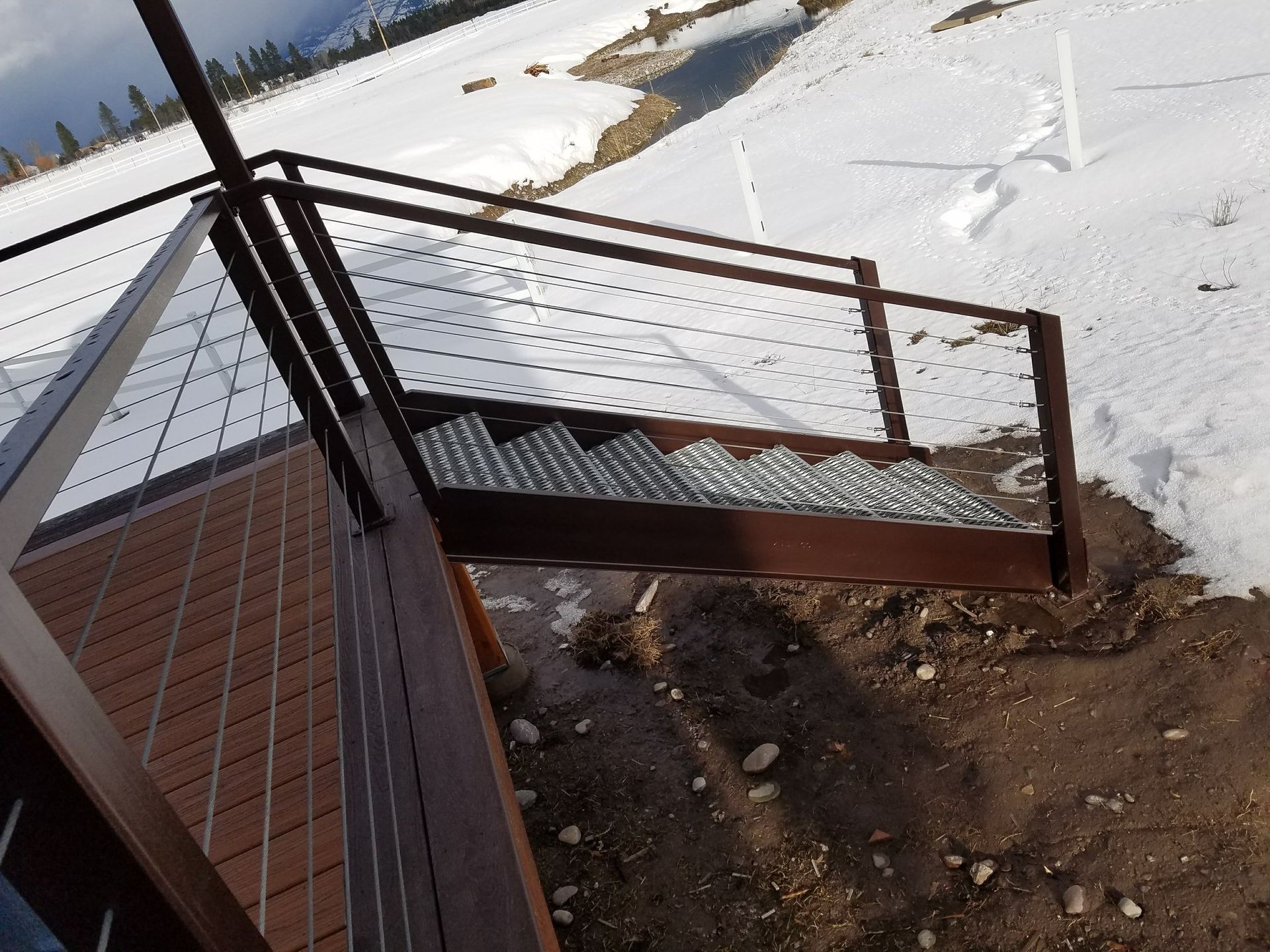 Metal staircase leading down from a wooden deck, surrounded by snow-covered ground.