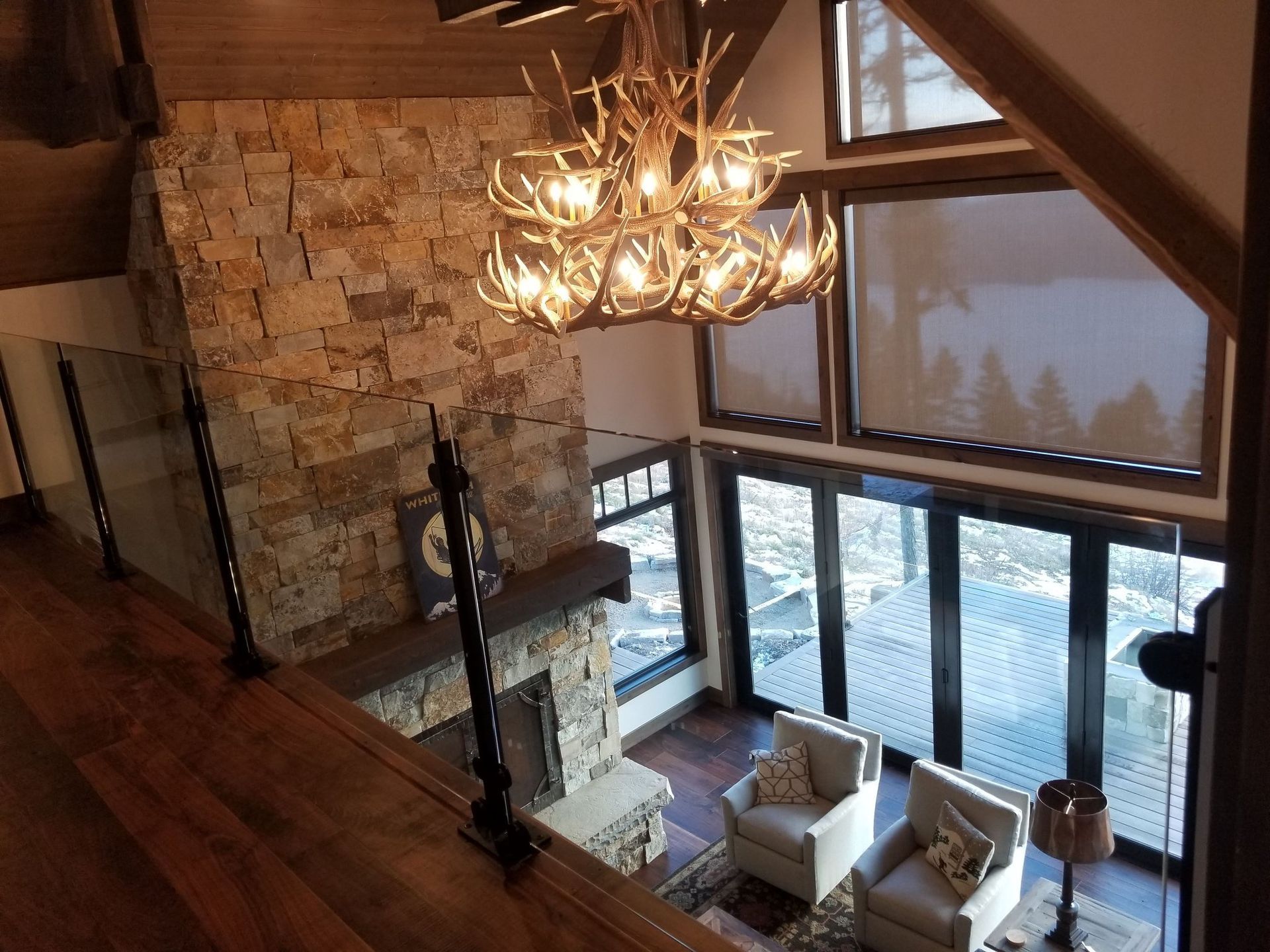 Stone fireplace, antler chandelier, and seating area in a rustic, well-lit cabin.