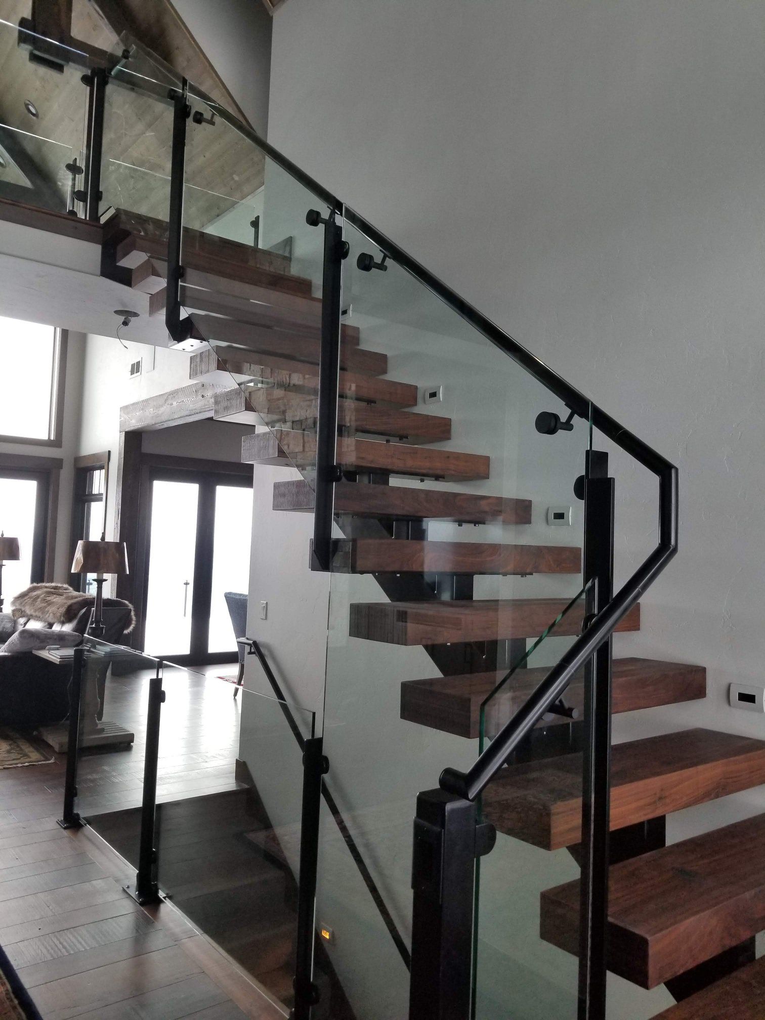 Floating wooden staircase with black metal railings and glass panels in a modern home.