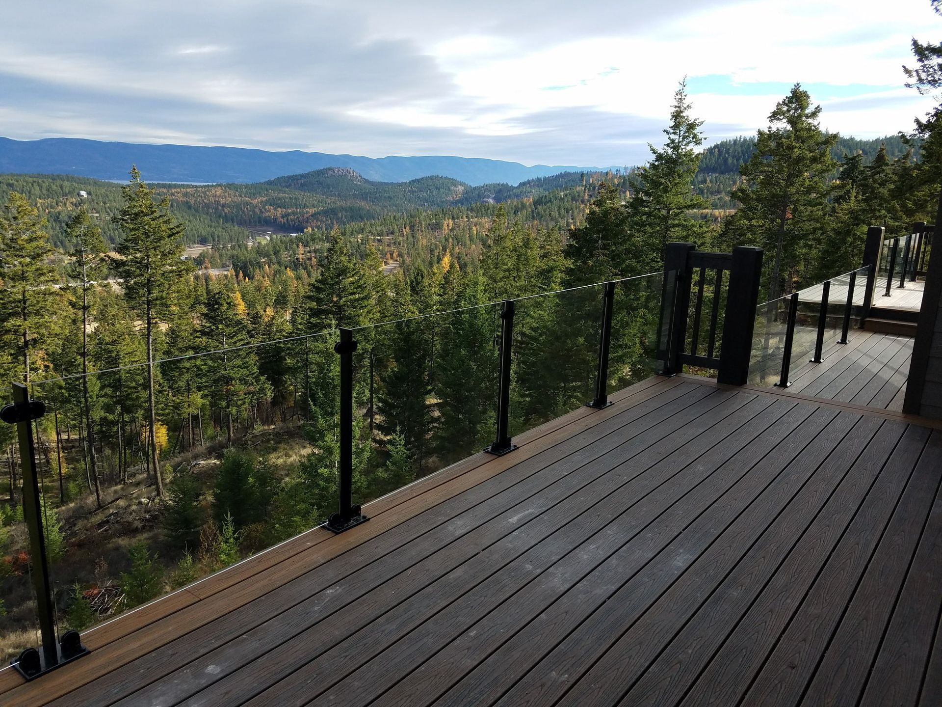 Wooden deck with glass railings overlooking a forested mountain landscape.